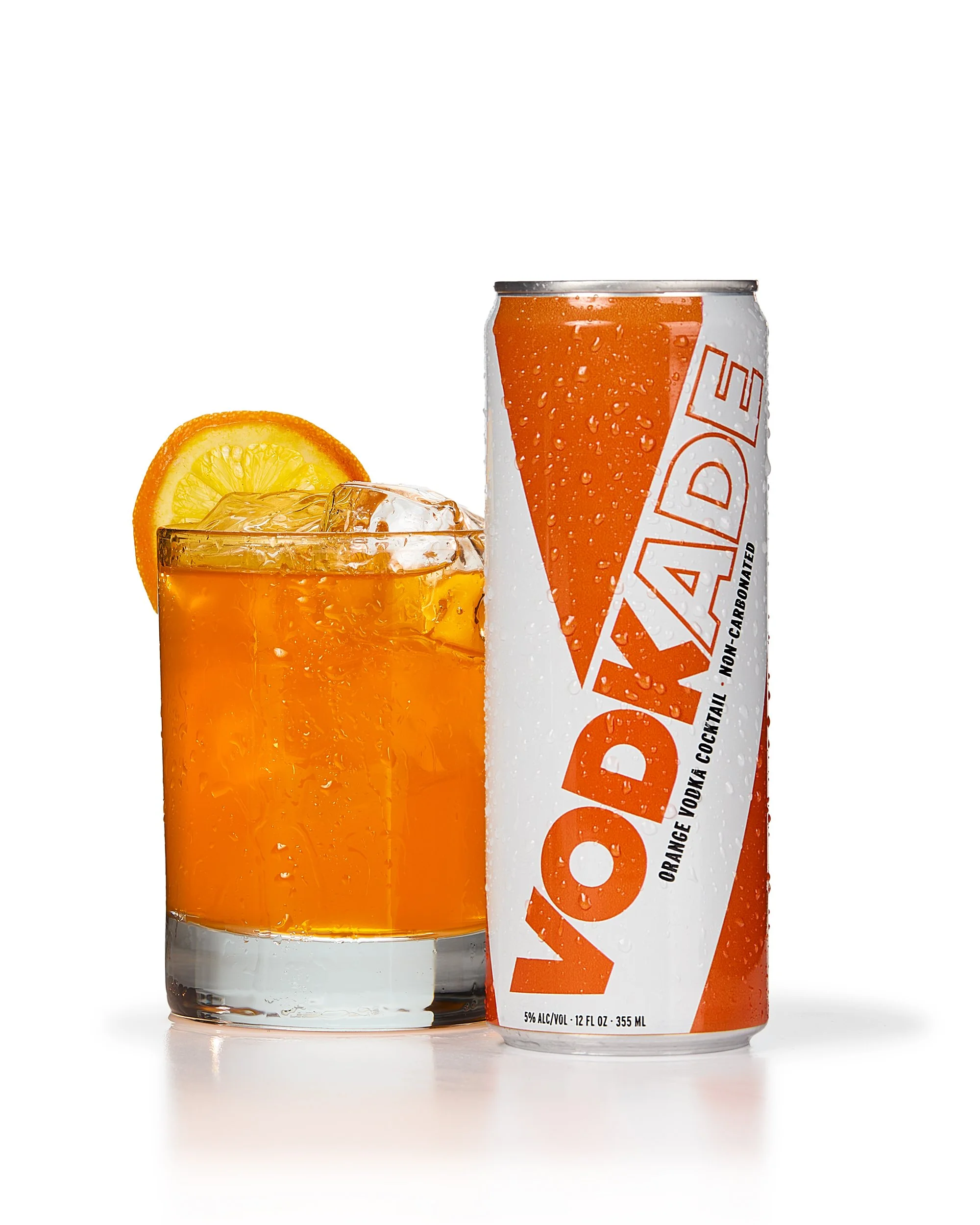 Orange-flavored vodka cocktail in a can, with a glass of iced drink garnished with an orange slice.