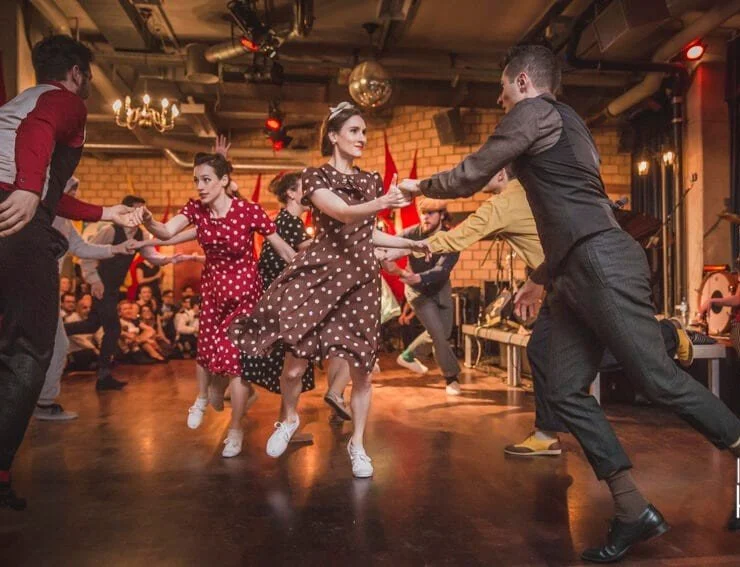 Mensen dansen vintage stijl in een gezellige, gezellige zaal met mensen die toekijken op de achtergrond.