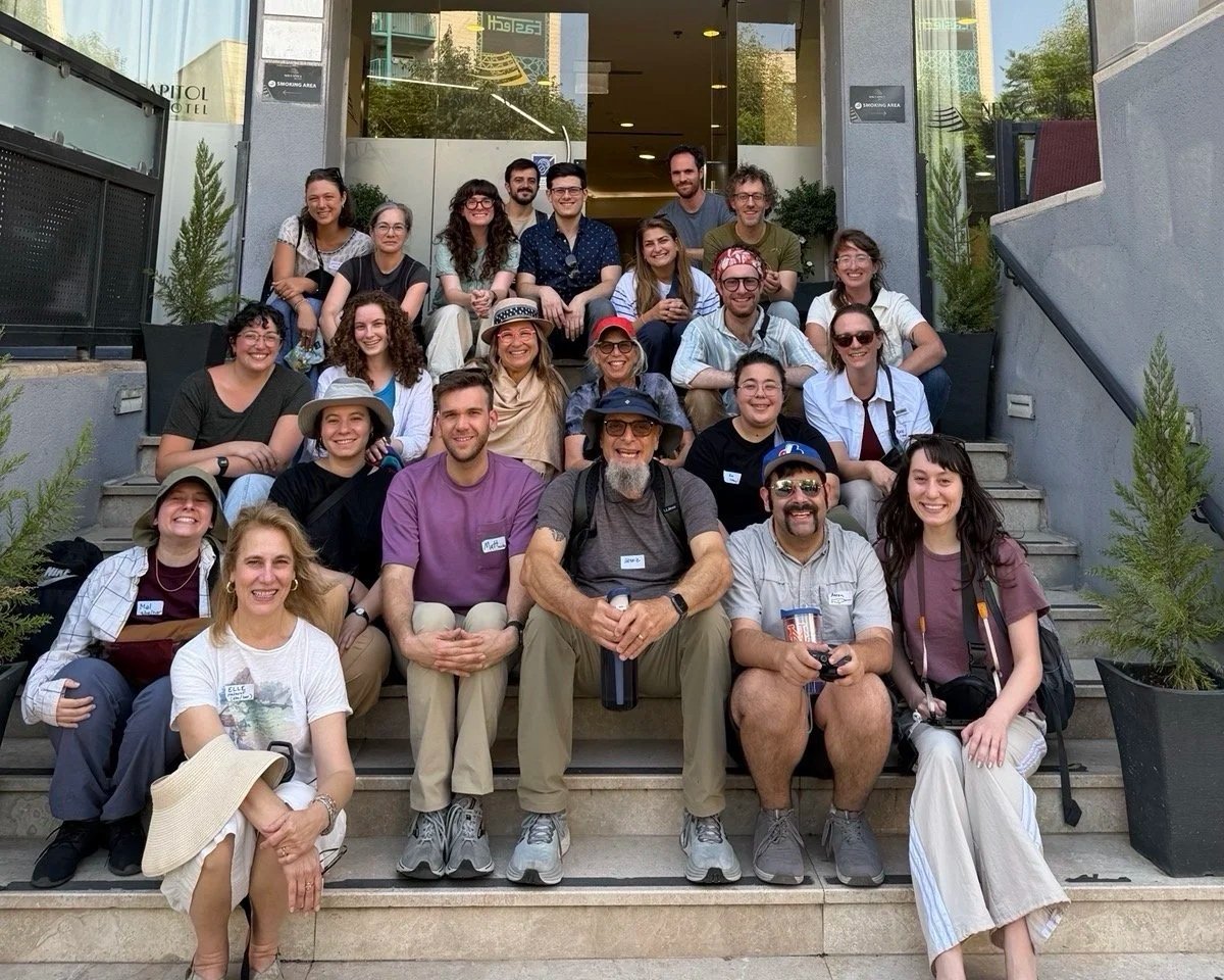 23 people sitting on a set of steps, smiling at the camera.