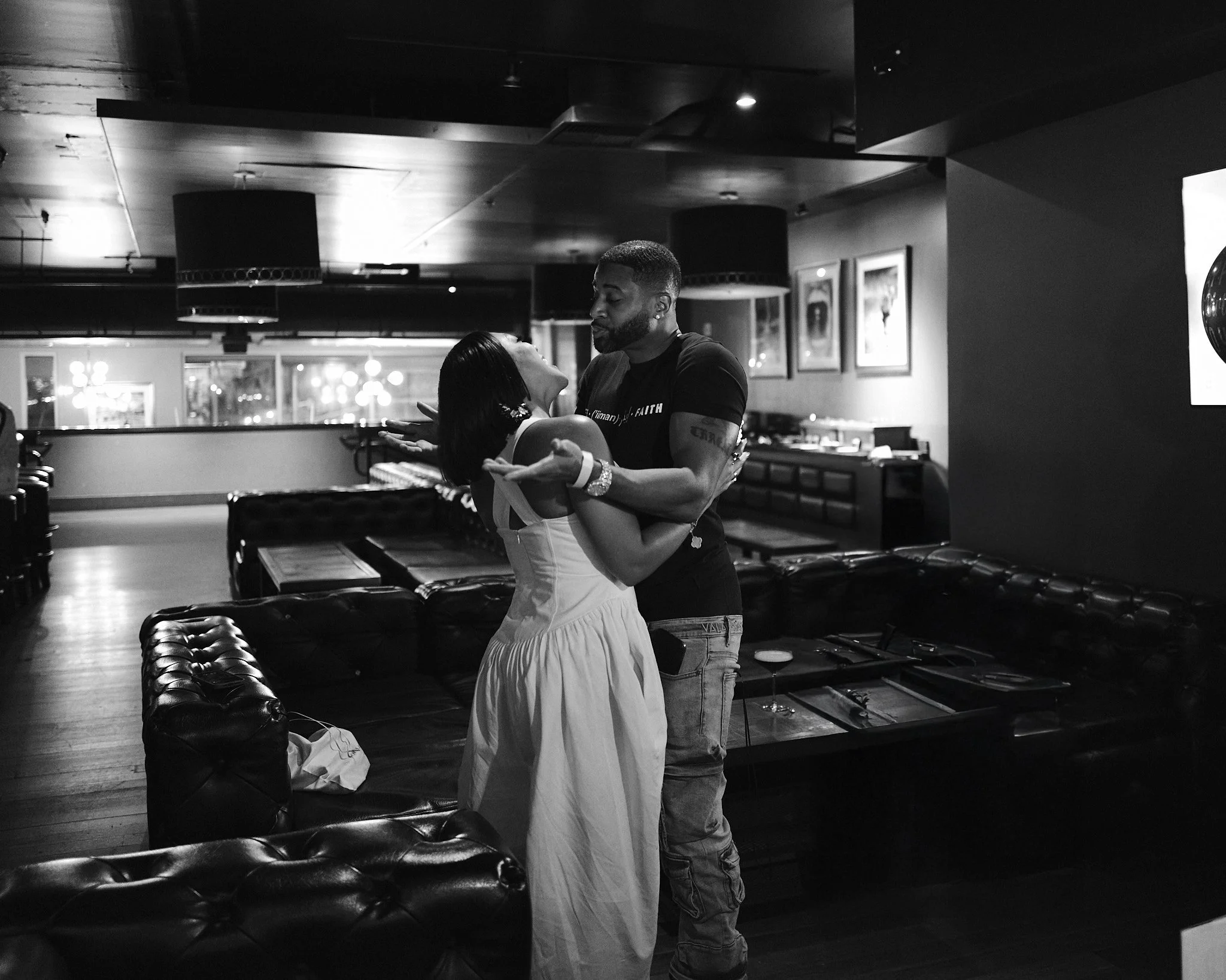 Devale and Khadeen dance closely in a dimly lit restaurant or lounge, with the woman looking up at the man, both holding hands. The background shows framed pictures on the wall and a bar or serving area.