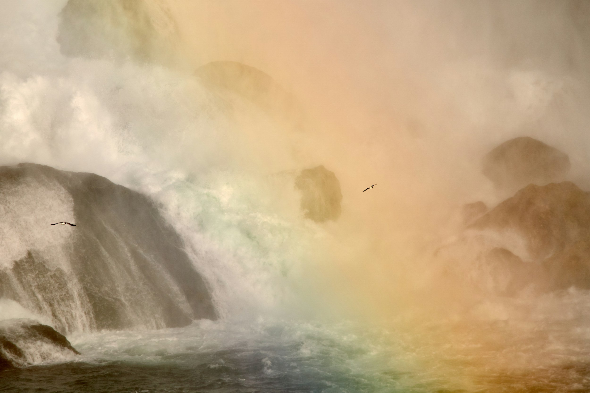 Waterfall with mist, rocks, and two birds flying in the sky.