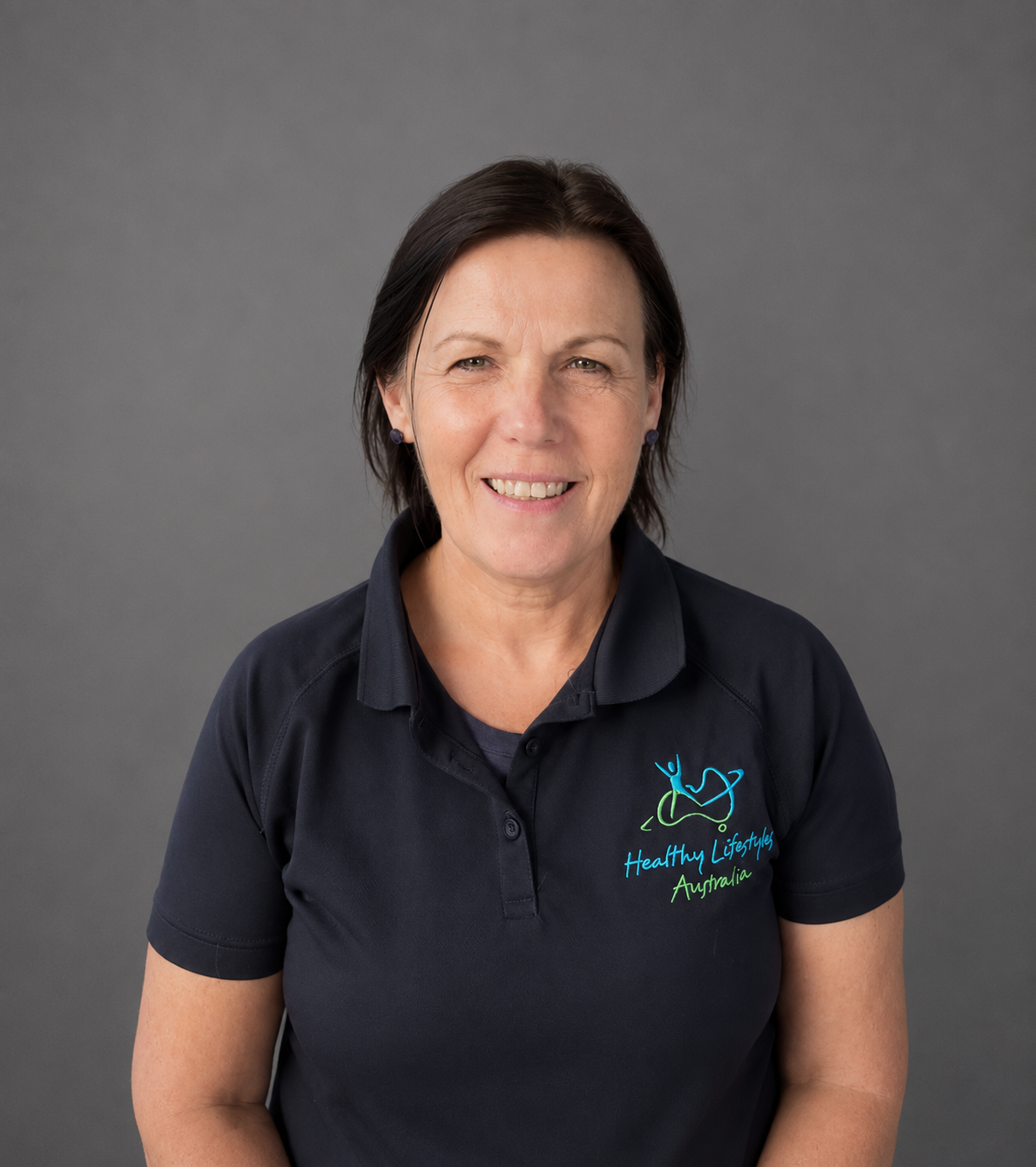 Person smiling, wearing a "Healthy Lifestyles Australia" shirt, standing in front of a textured wall.