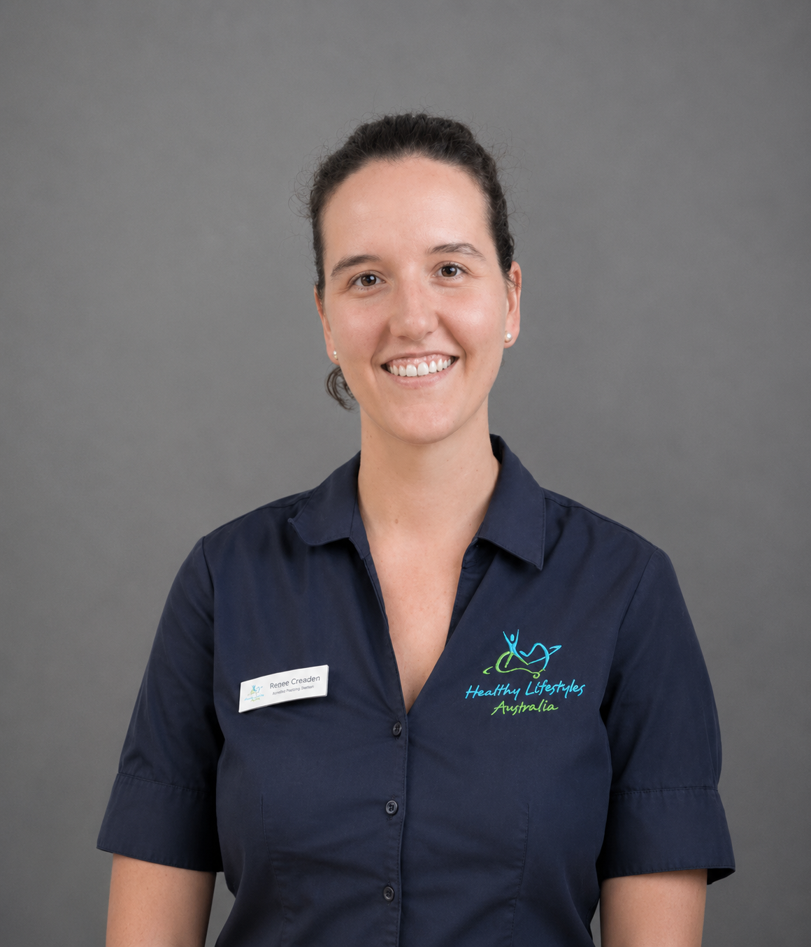 Person wearing a dark polo shirt with a name tag and "Healthy Lifestyles Australia" logo, standing in front of a textured wall.