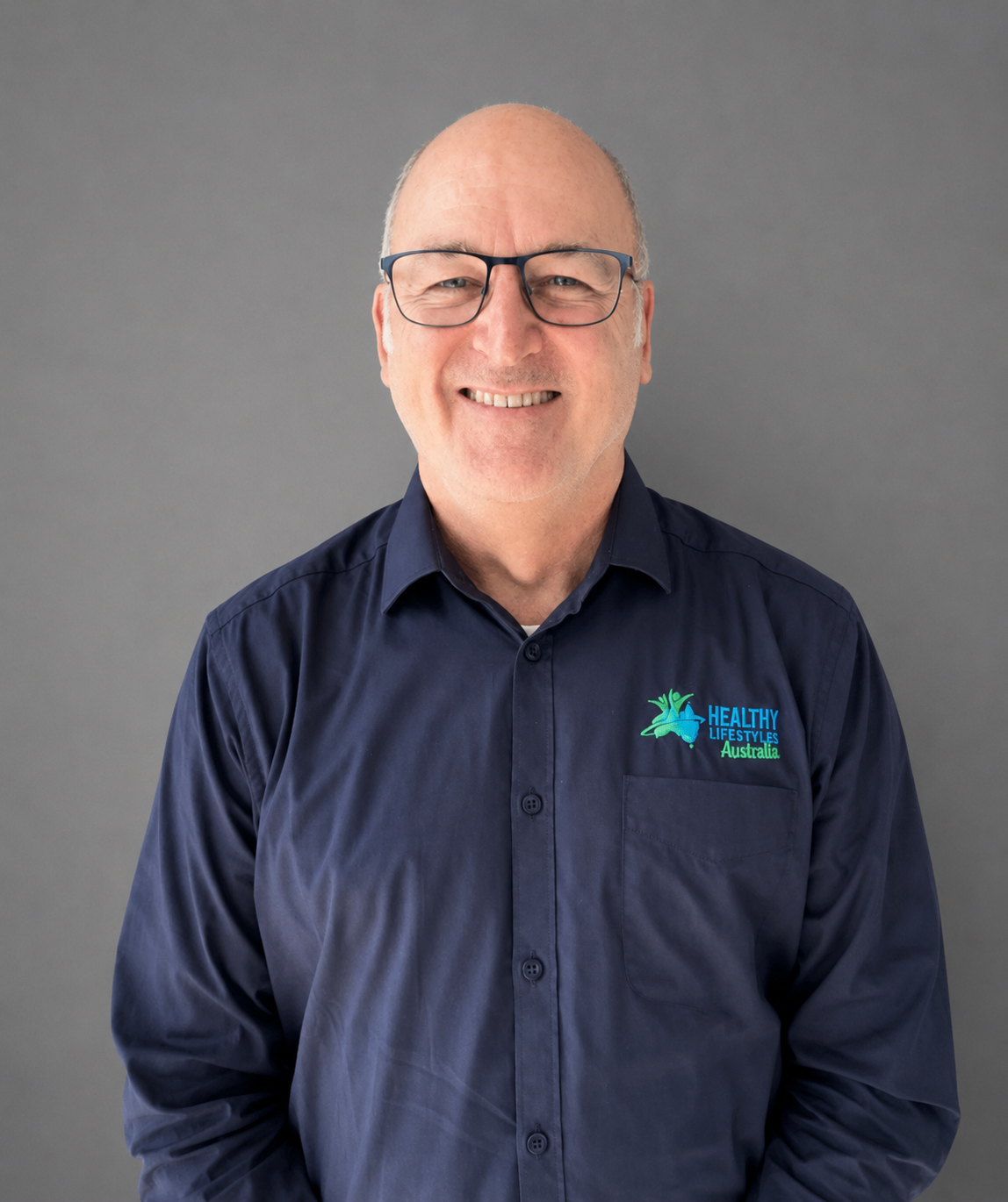 Man wearing glasses and a shirt with "Healthy Lifestyles Australia" logo, standing against a textured wall.