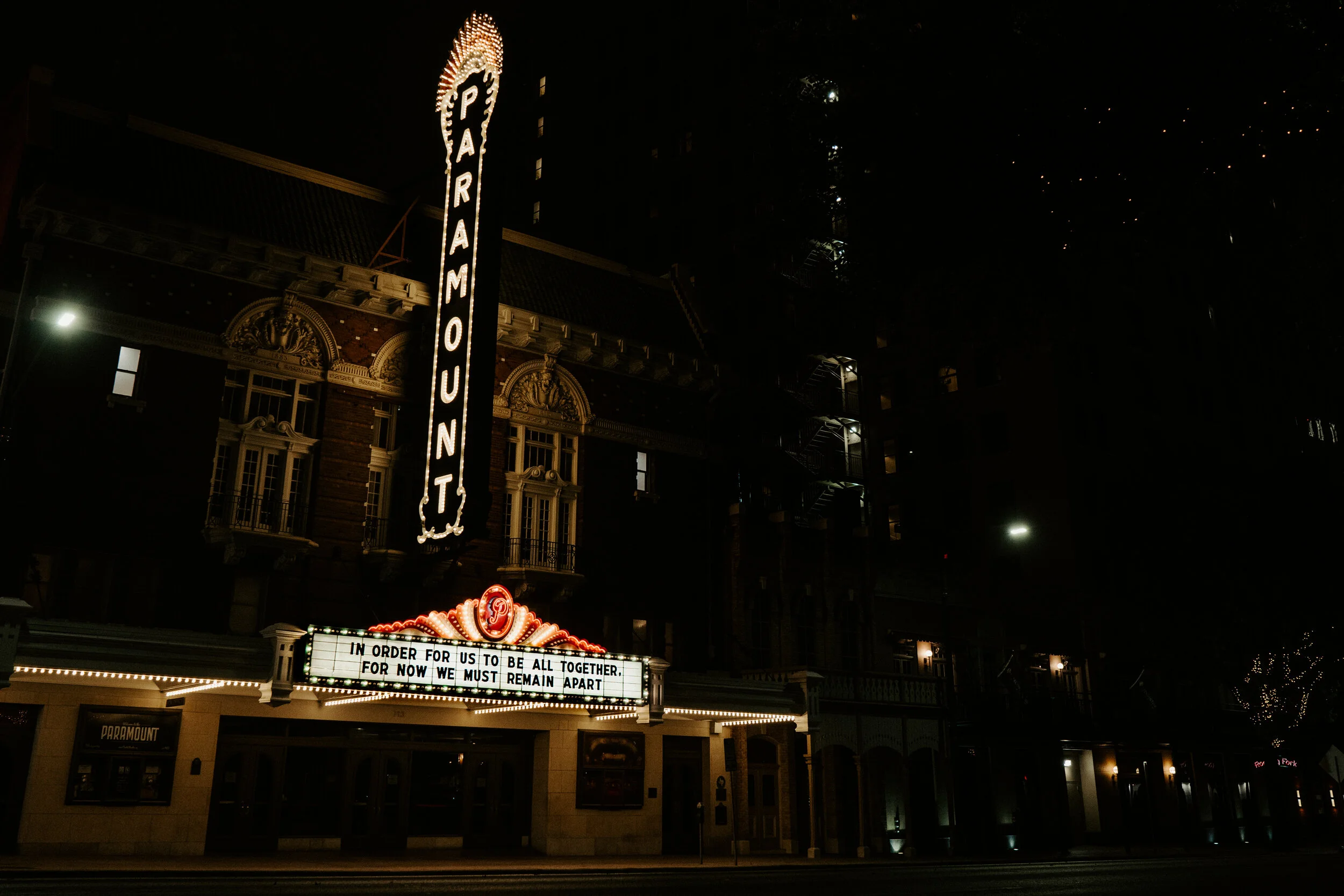 Nighttime view of the Paramount Theater with illuminated marquee displaying a message about public health restrictions.