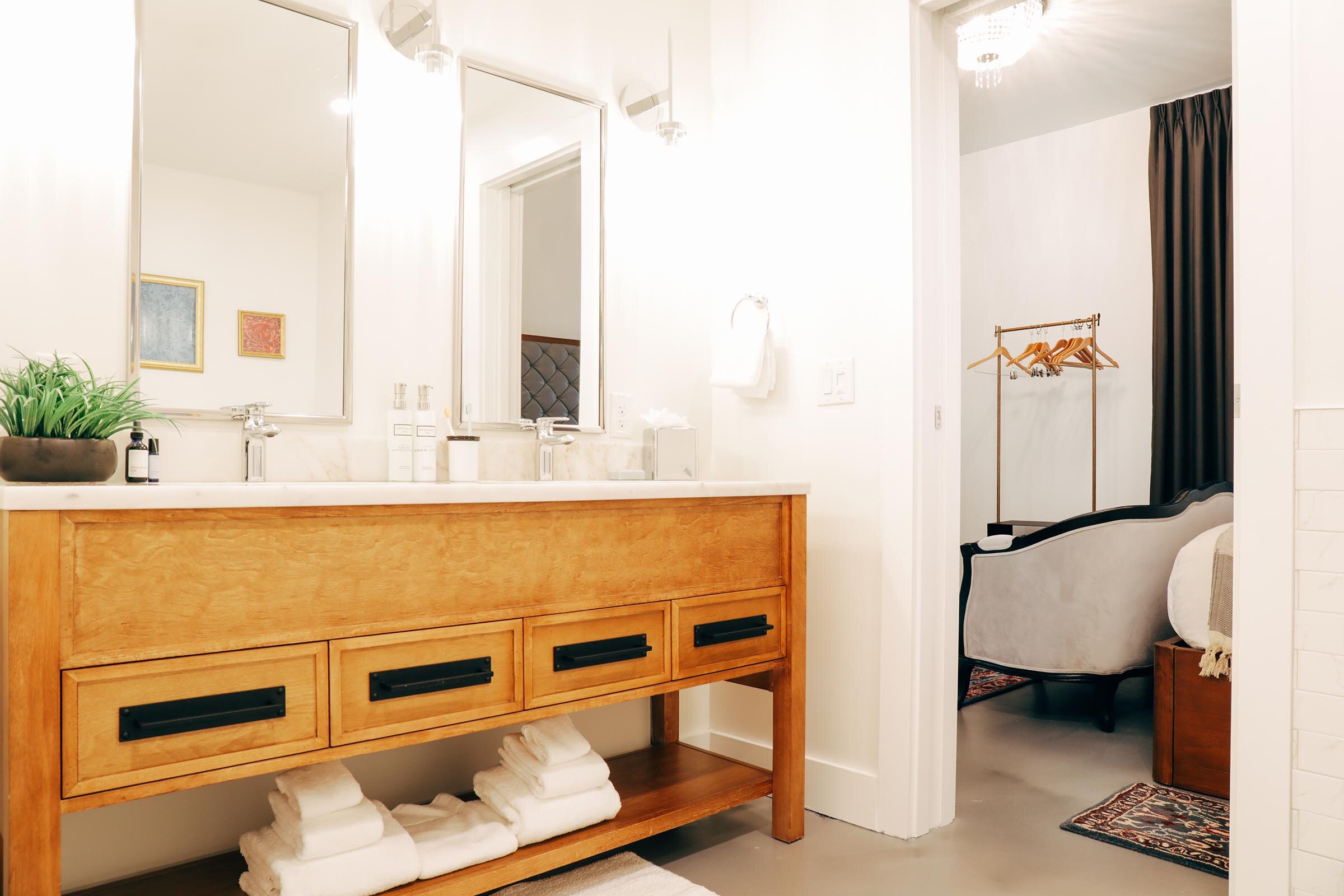 en suite bathroom with double sink vanity, wooden drawers, white countertop