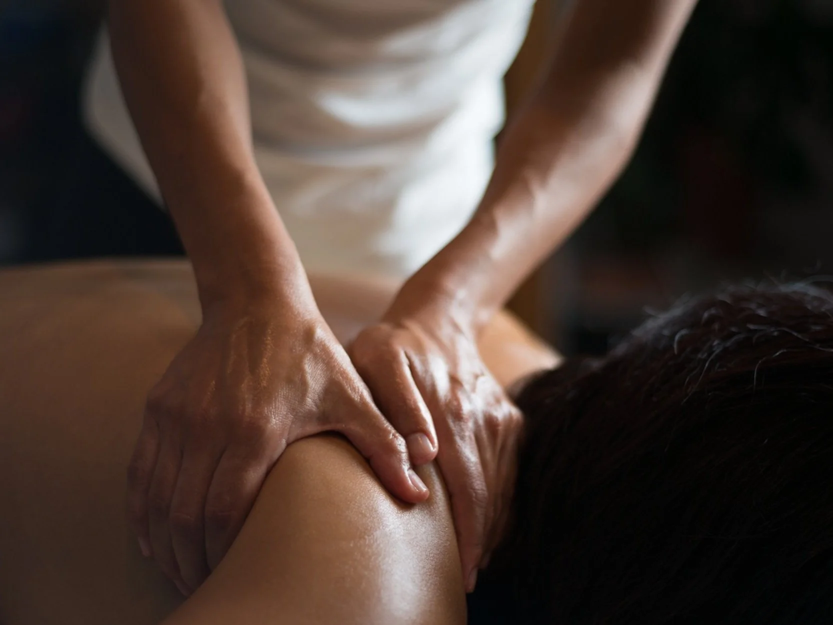 A person receiving a massage with hands applying pressure to the back and shoulder area.