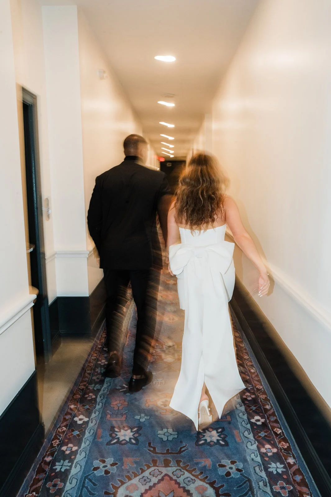 A woman in a white wedding dress walking down a hallway with a man in a black suit.