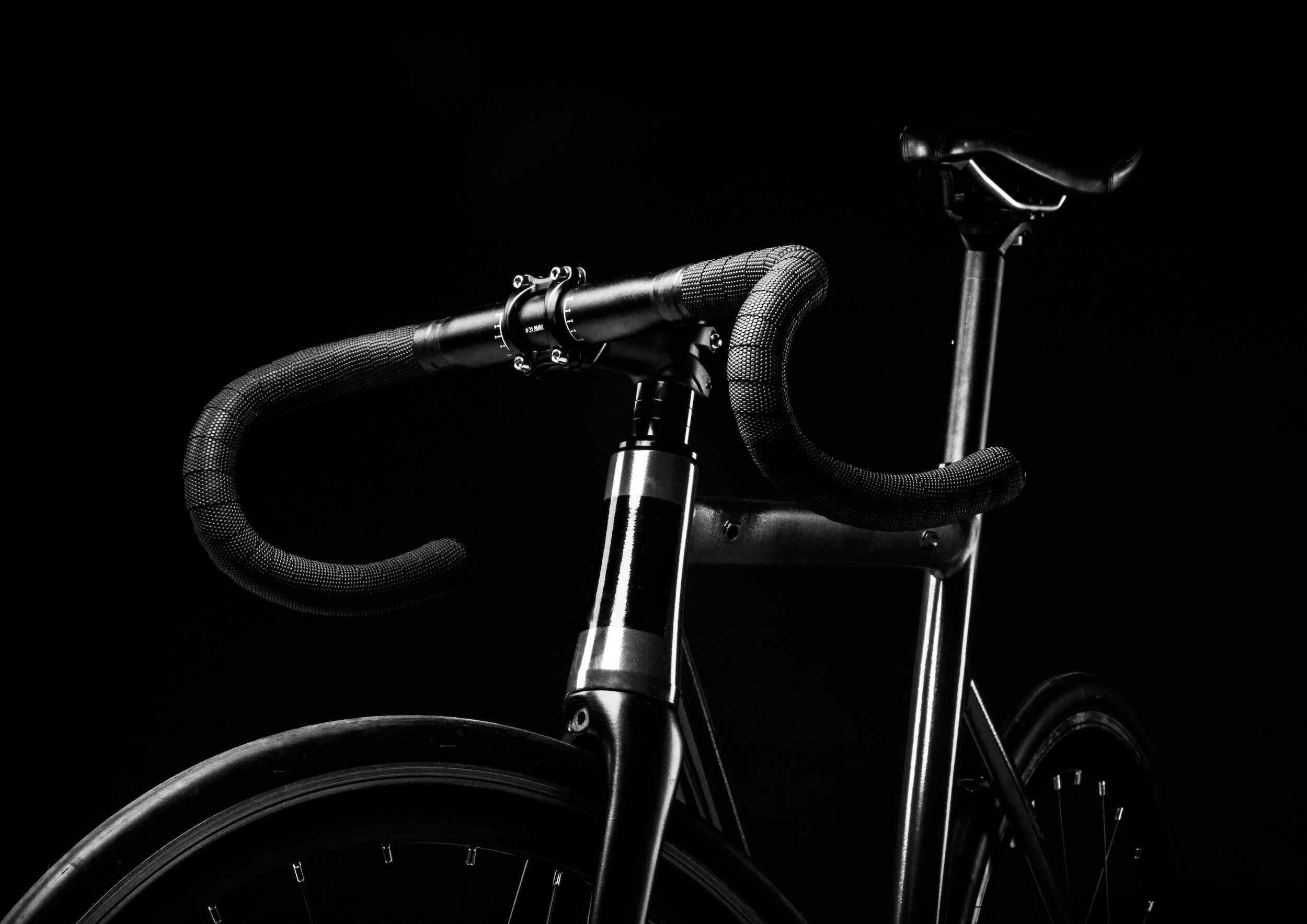 Modern black custom built bicycle on black background and zoomed into the handlebars. 