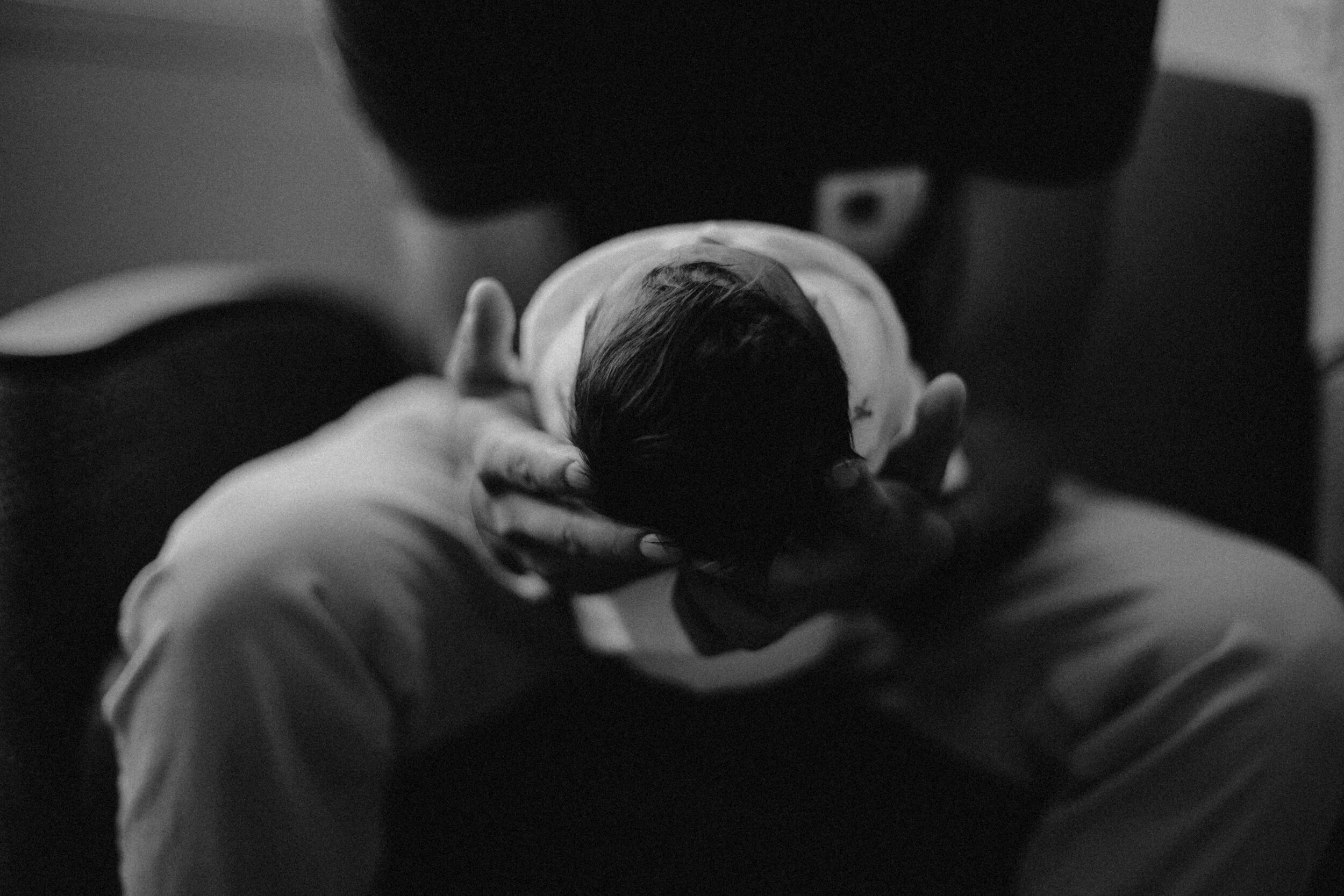 A person holding a newborn baby in black and white, viewed from above.