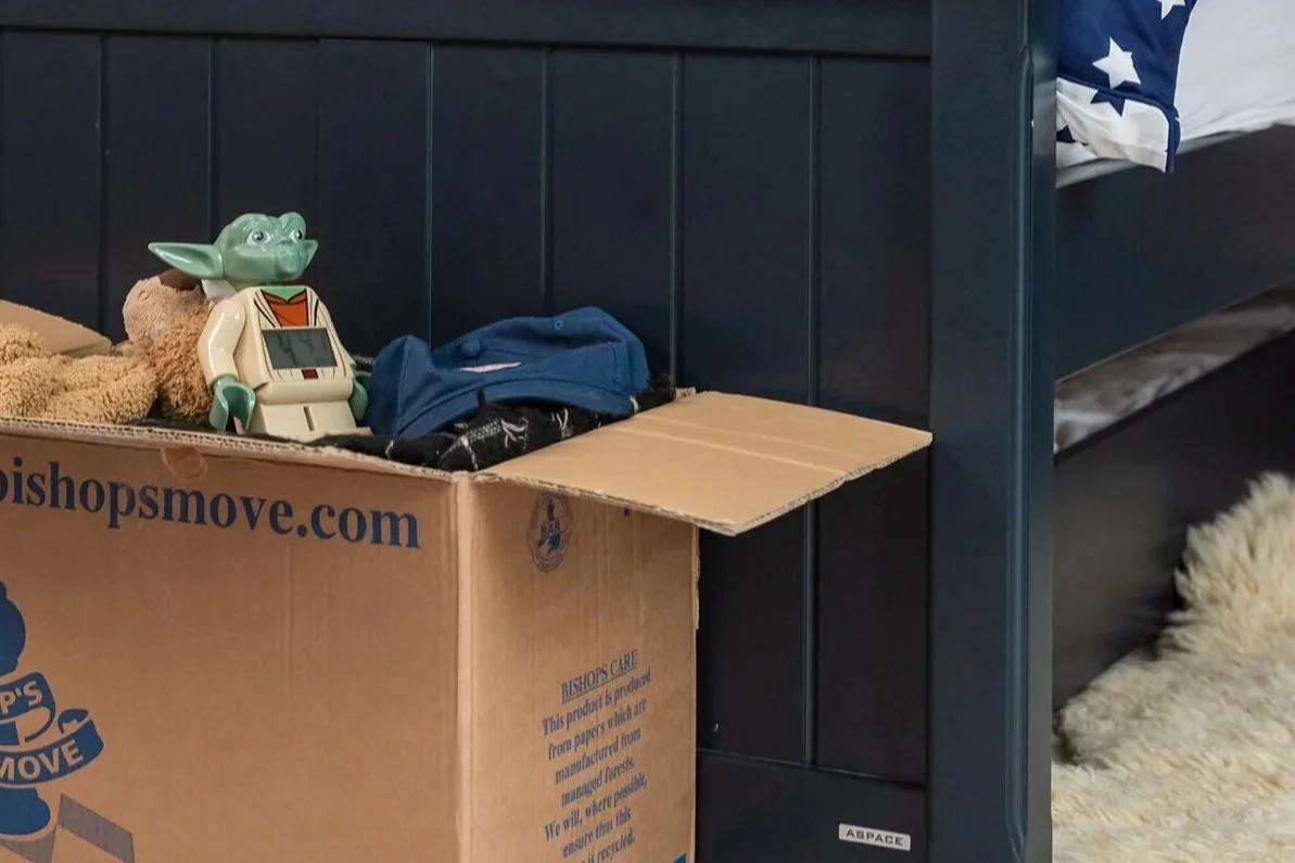 Personal belongings prepared for storage in a Bishop’s Move box beside a bed