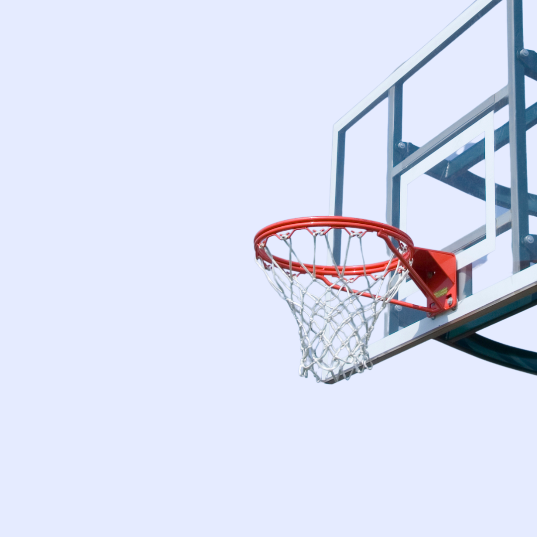 Basketball hoop with net on the side of a basketball court against a pale blue sky.