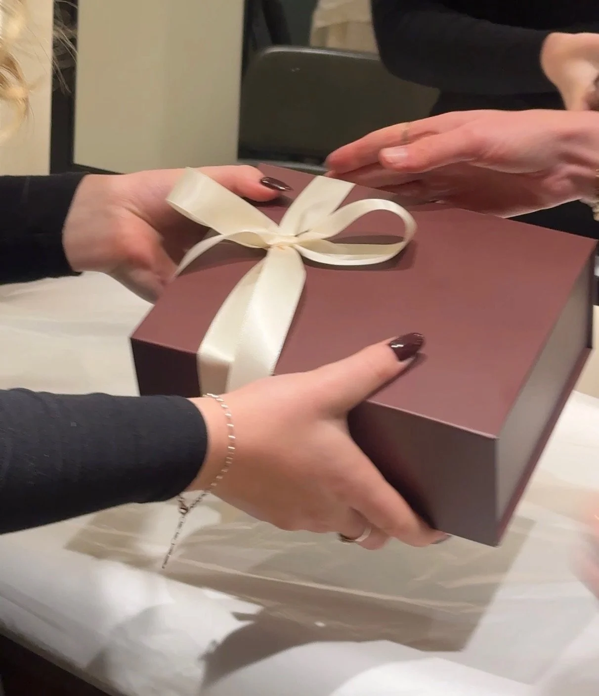 Hands exchanging a softly wrapped Christmas gift in a warm burgundy box with a cream ribbon at Carmen Walker Hair, Leamington Spa.