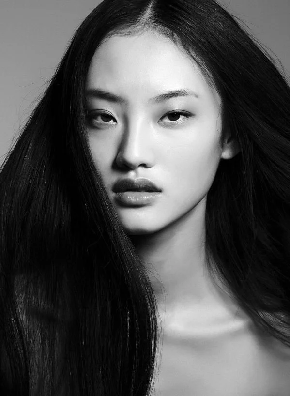 Black and white portrait of an Asian woman with long, straight hair, looking directly at the camera with a serious expression.