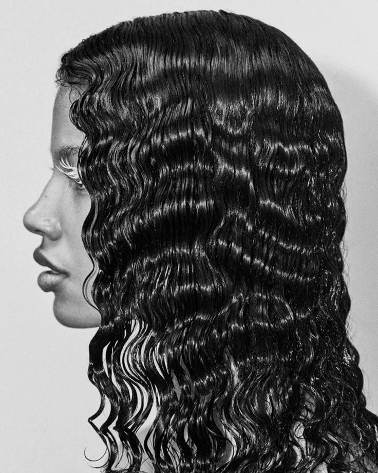 A black-and-white photo of a woman in profile with long, curly, wet-looking hair.