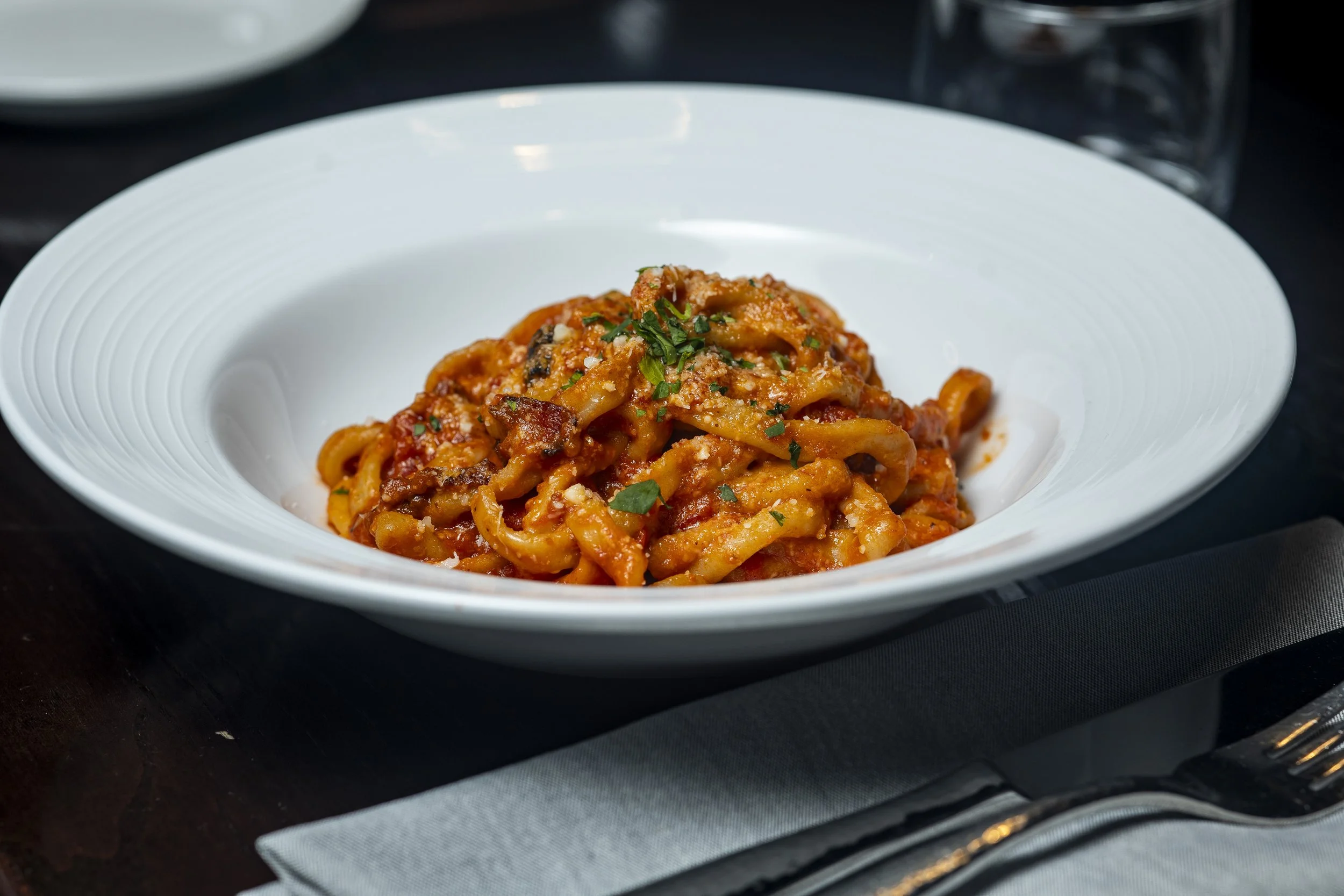 A bowl of Italian pasta with tomato sauce and garnished with chopped herbs.