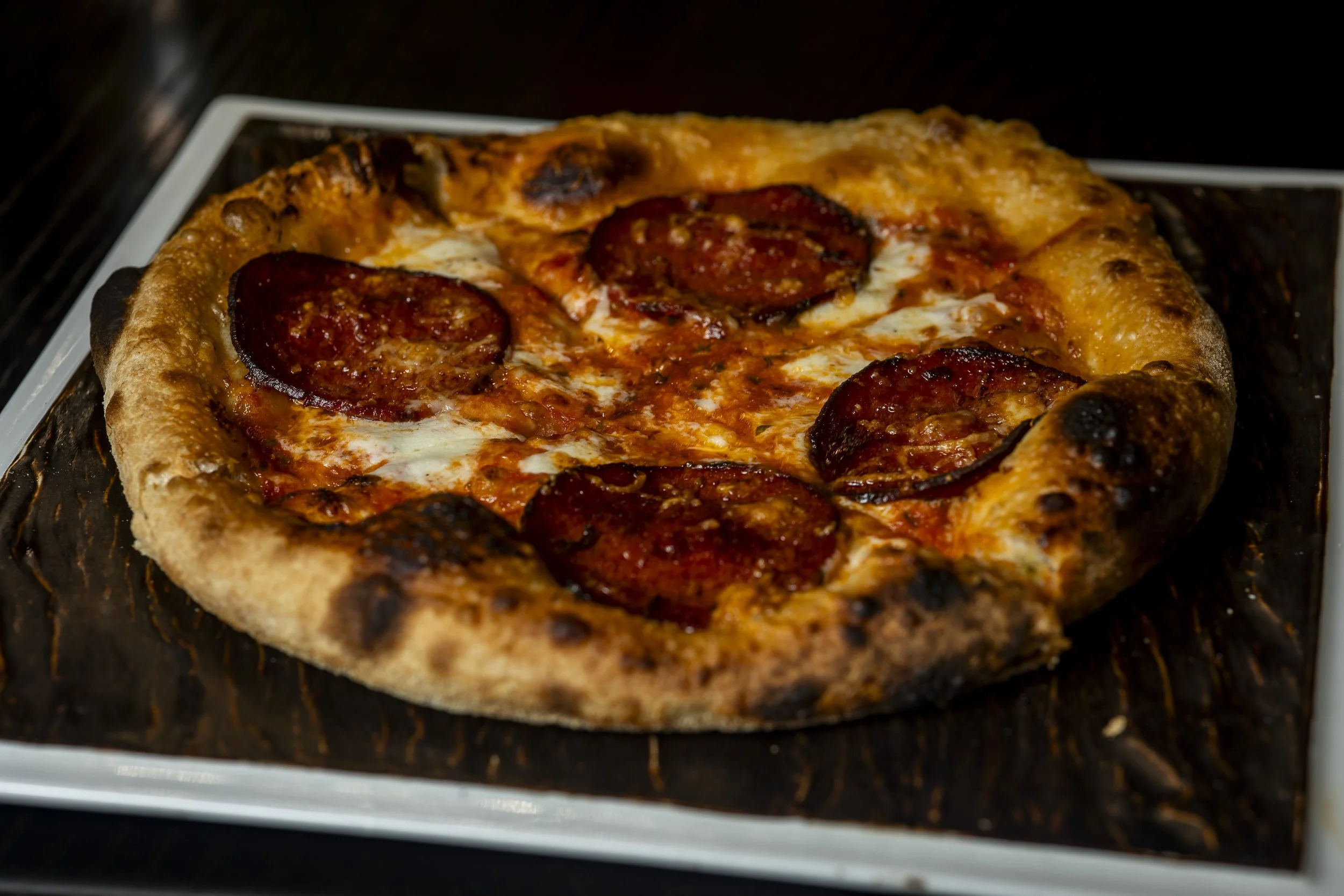A pepperoni pizza with a thick crust on a black tray.