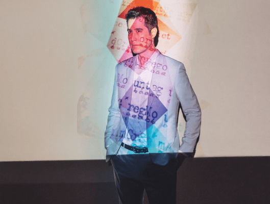 man in a gray suit with colorful shapes and text projected on him