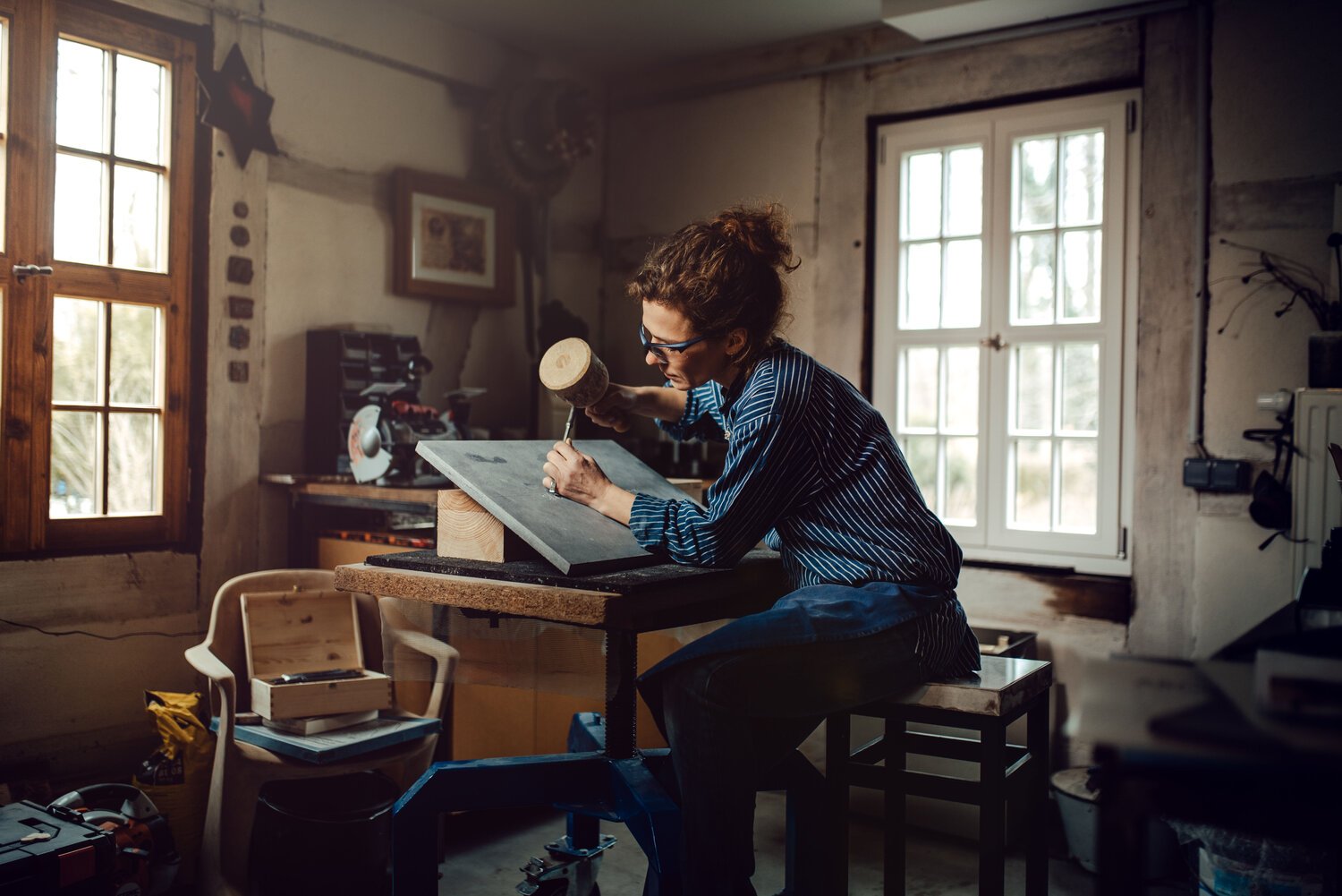 Eine Frau arbeitet in einer Werkstatt, sie schnitzt Holz mit einem Hammer und einem Meißel. Employer Branding hautnah.
