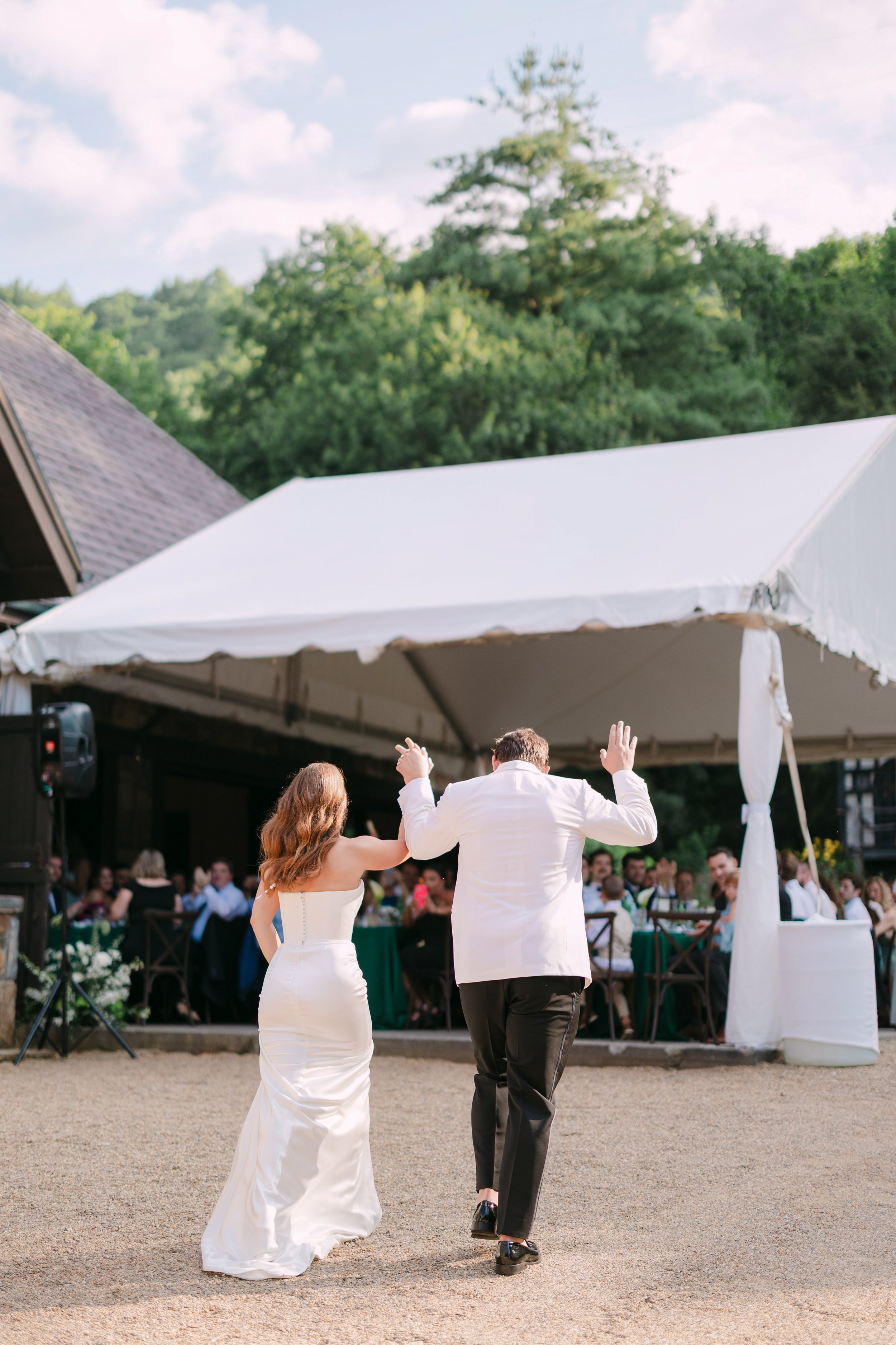 A bride and groom dancing at their outdoor wedding reception under a white tent with seated guests watching.