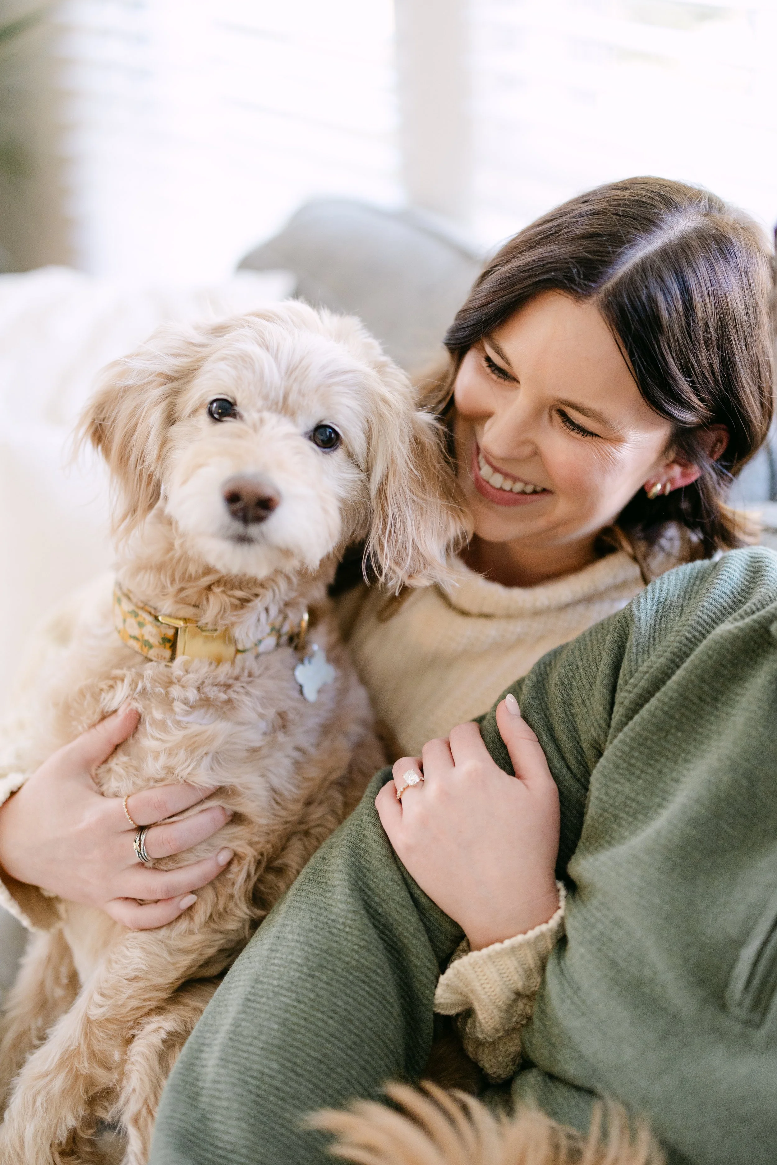 A woman smiling while holding a light brown, fluffy dog.