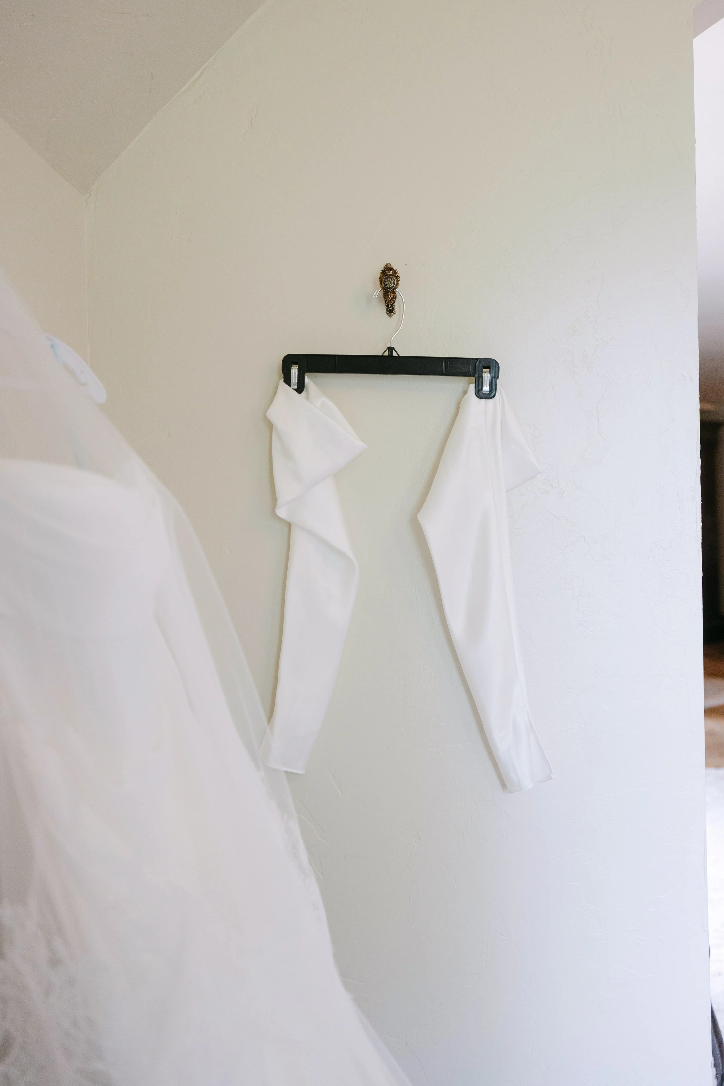 White fabric hanging on a hanger attached to a wall, possibly a wedding dress or similar garment.