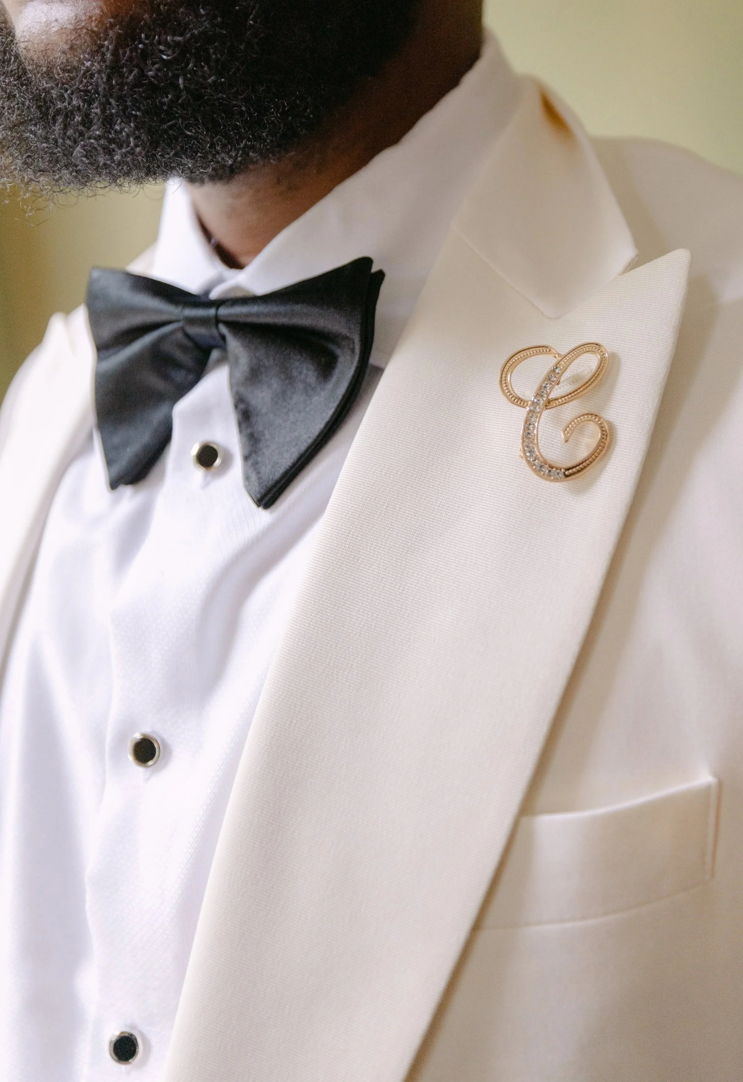 Groom wearing a white tuxedo with a black bowtie and a gold brooch.