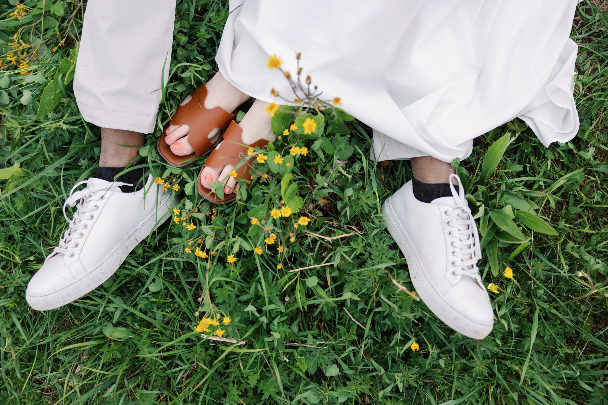 Person lying on grass with yellow flowers, white shoes, white pants, and a white shirt.