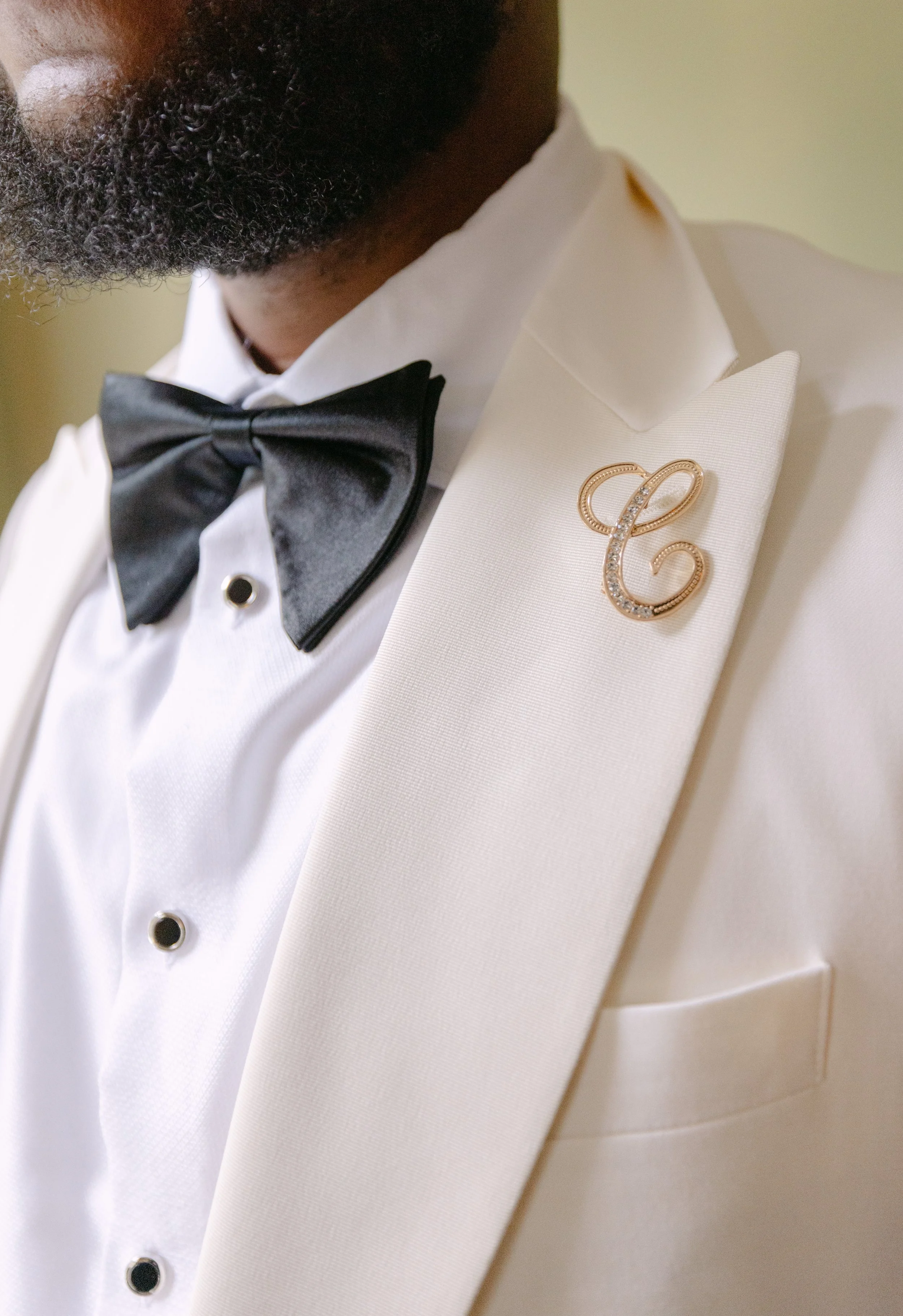 Close-up of a man wearing a white tuxedo with a black bowtie and a gold brooch.