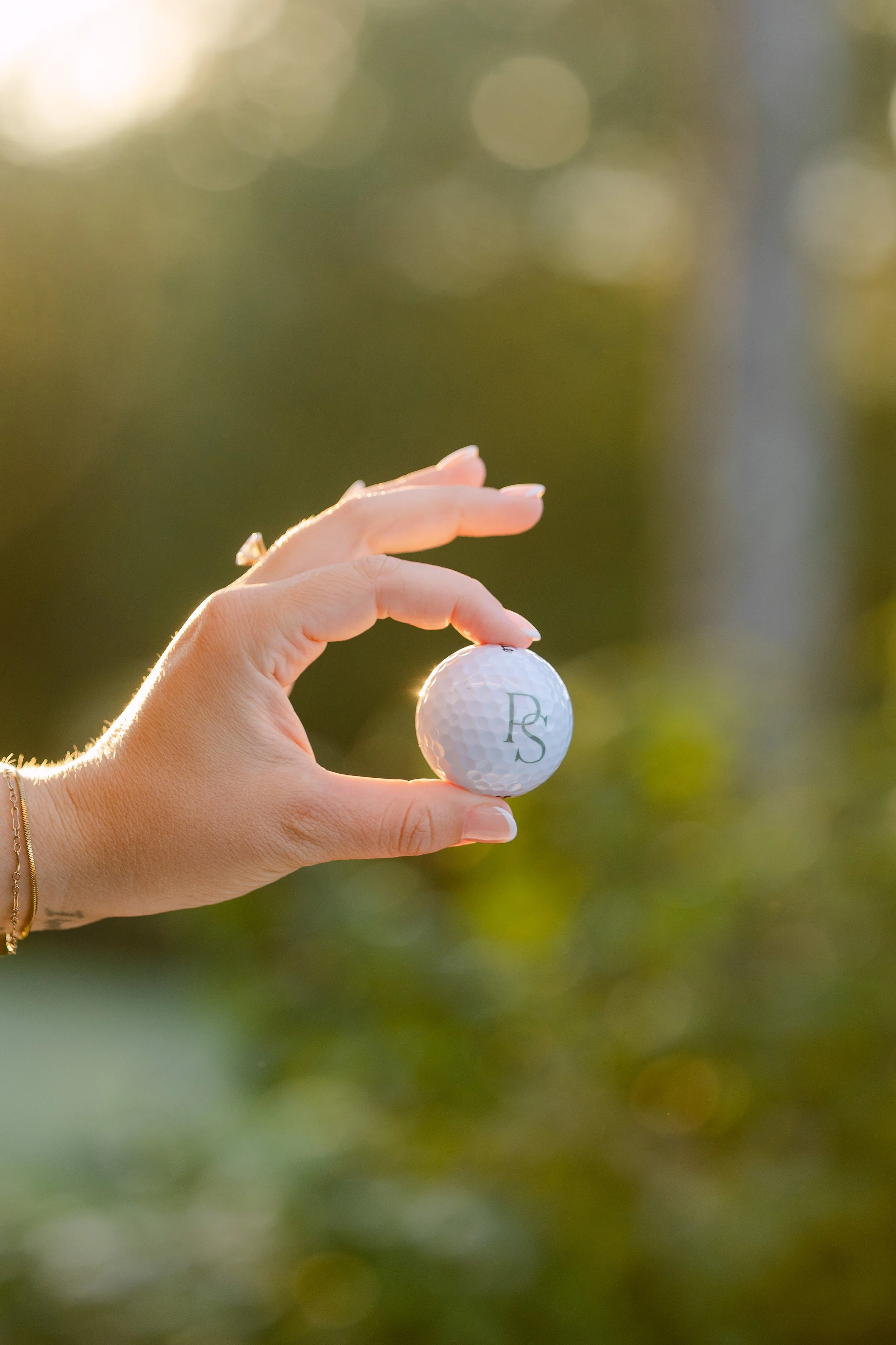 A hand holding a golf ball with the initials 'RS' engraved on it against a blurred outdoor background.