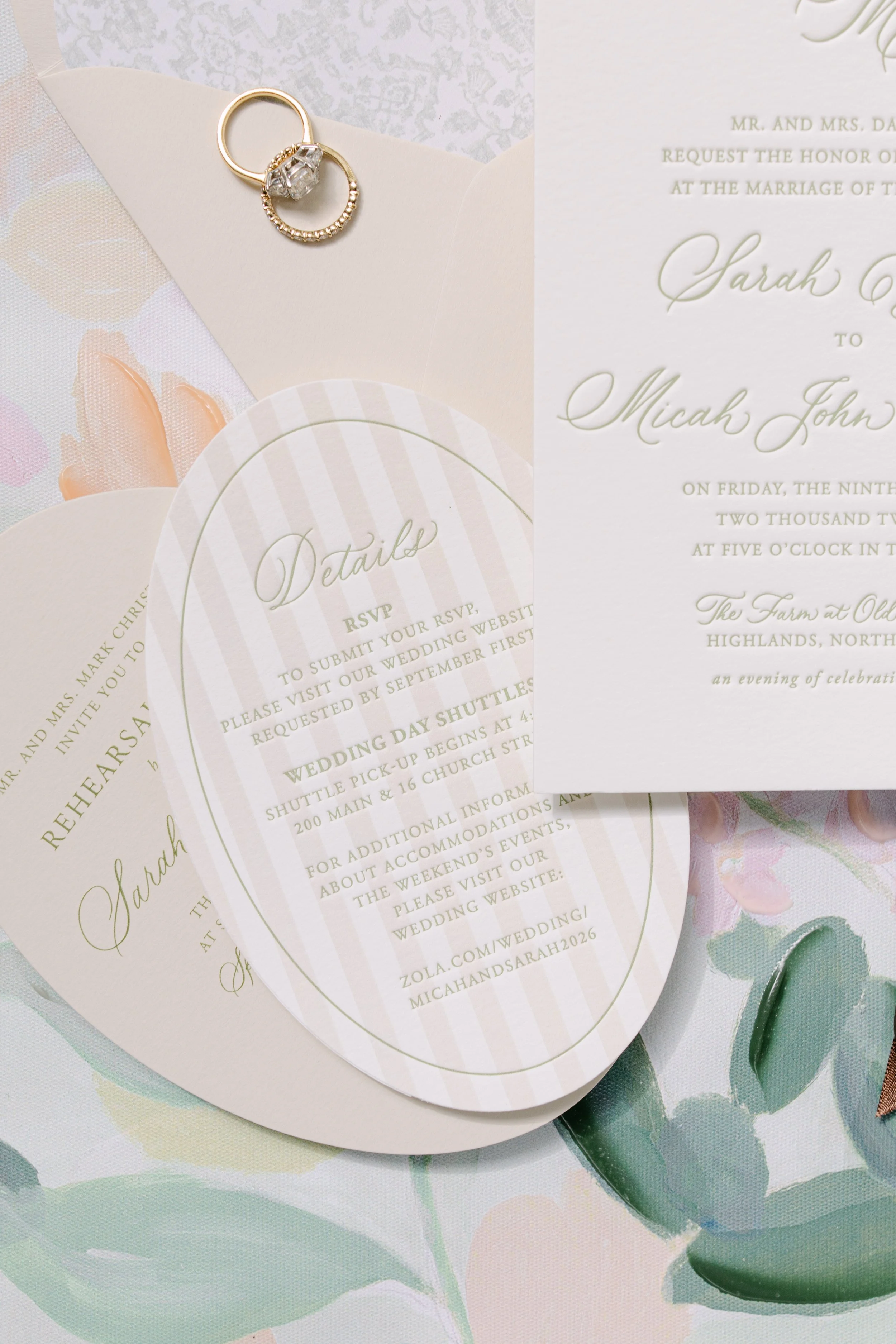 Gold wedding rings resting on pastel wedding invitations and RSVP cards with floral stationery.