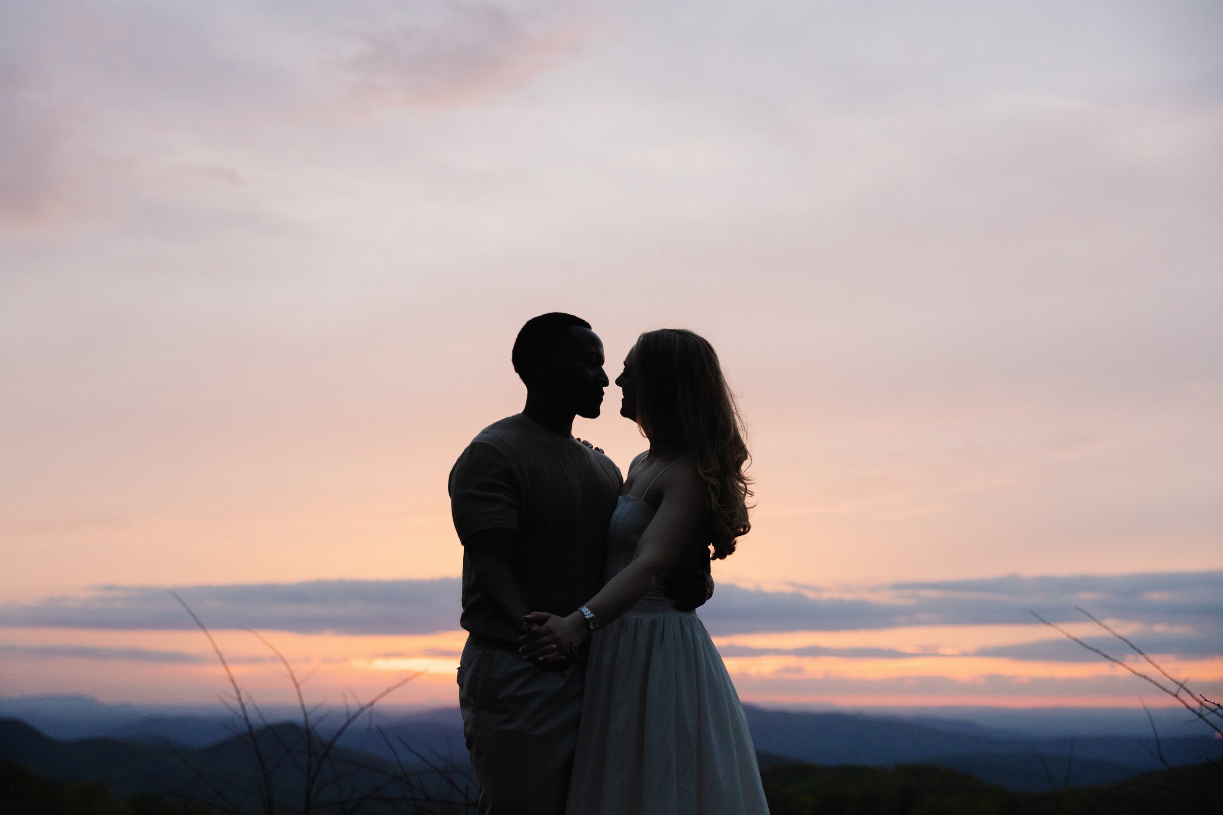 A silhouette of a couple embracing at sunset on a mountain overlook.