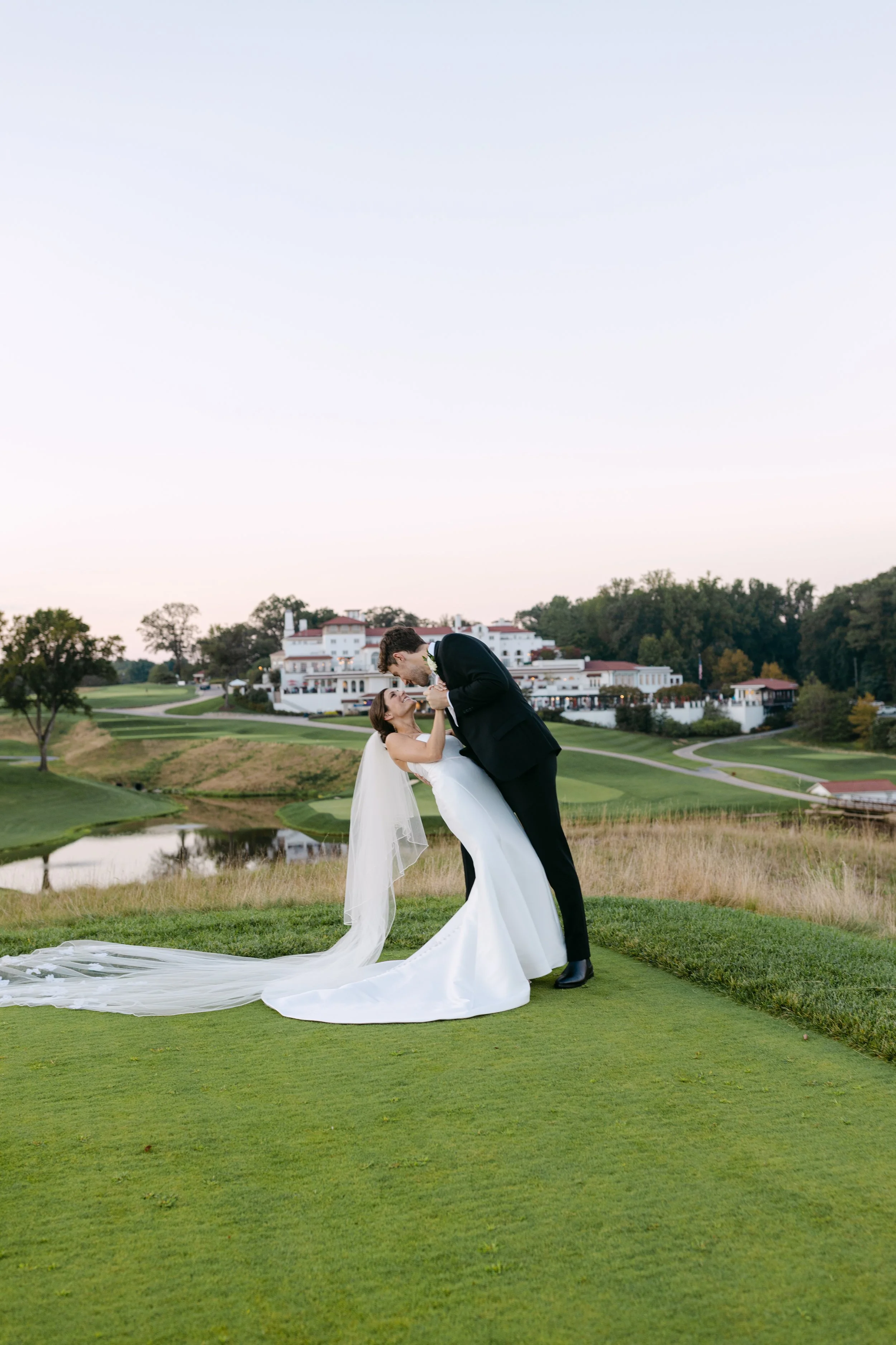 A bride and groom sharing a romantic dance on a golf course with a scenic landscape and large hotel in the background.