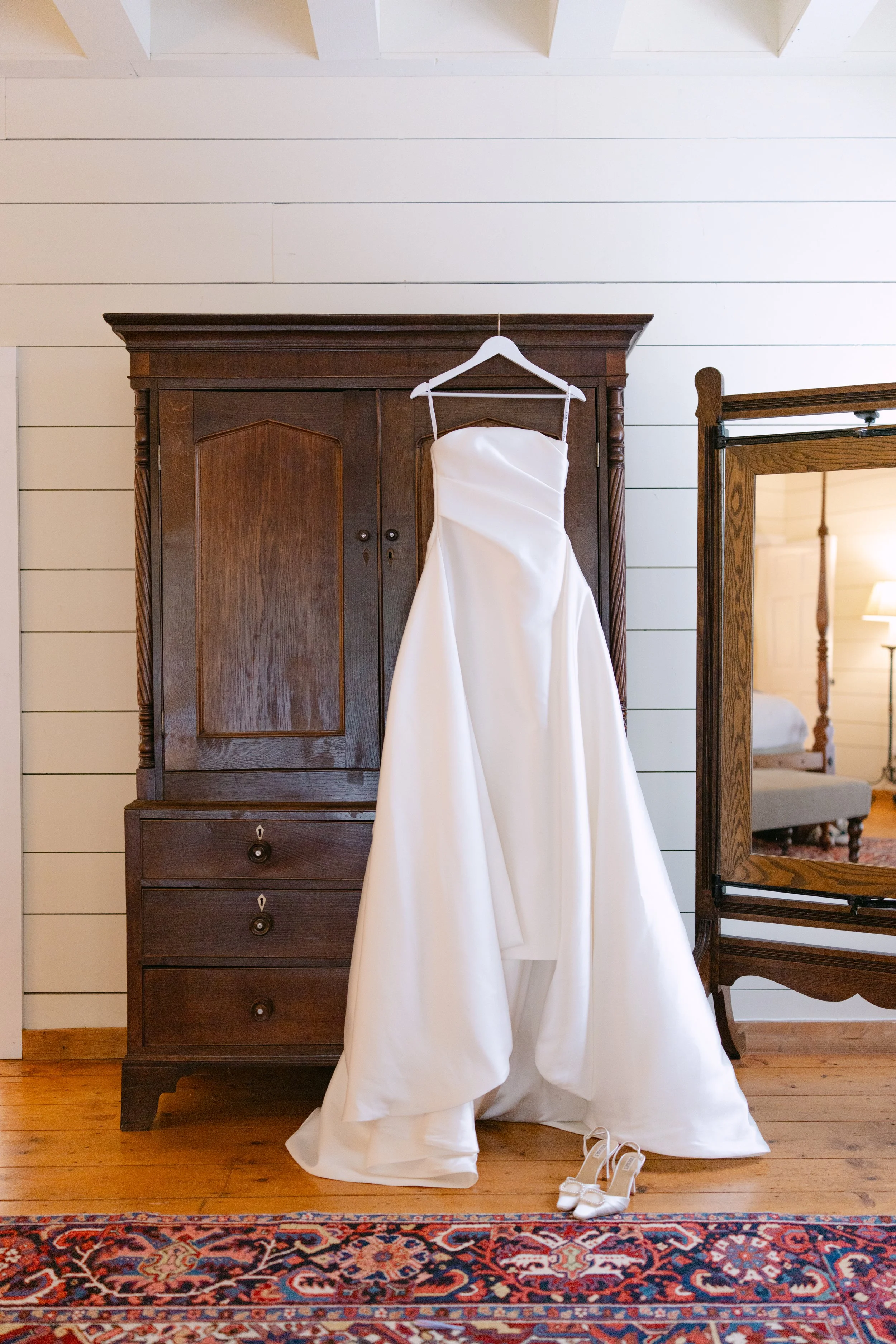 White wedding dress and matching shoes displayed in front of an antique wooden wardrobe