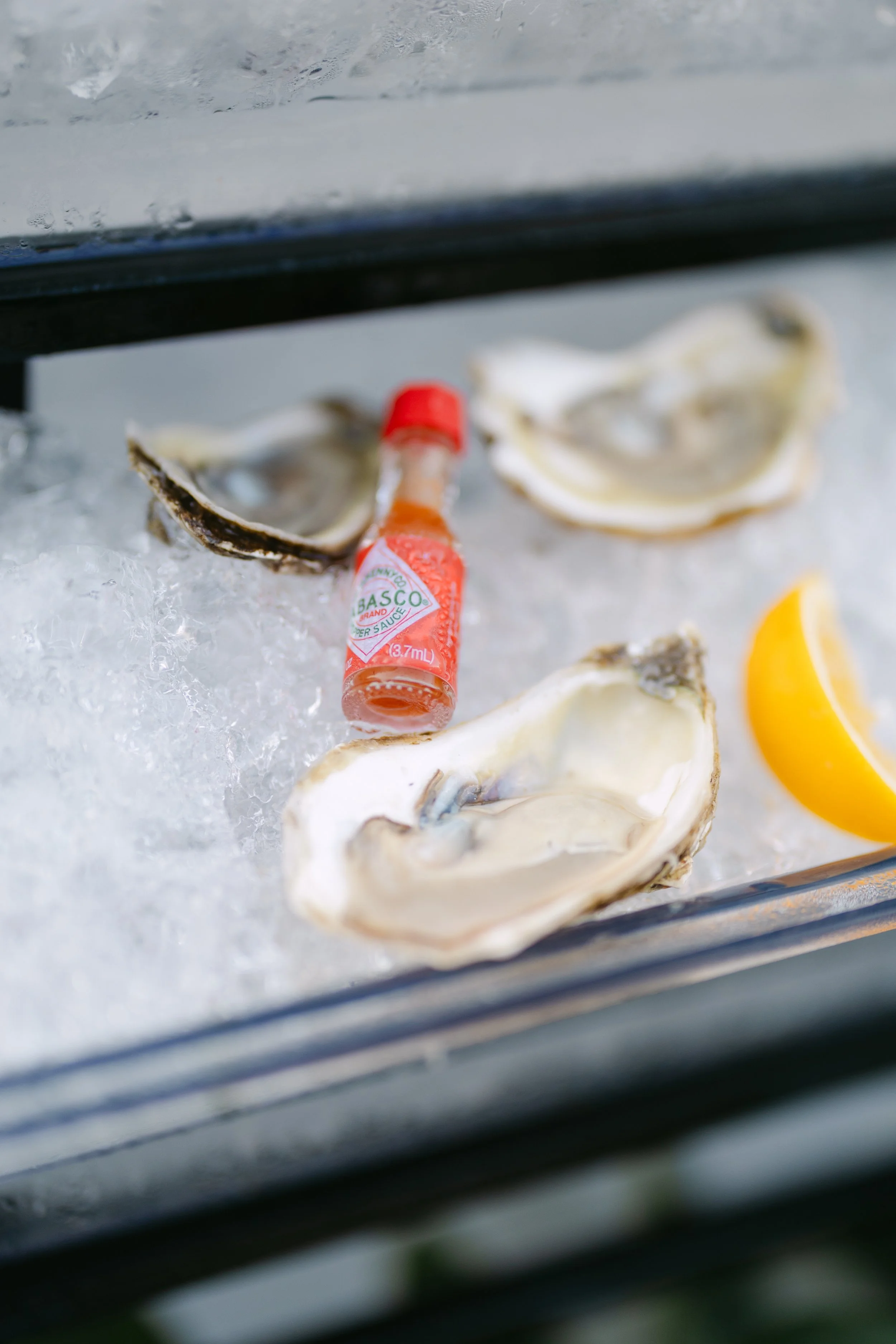Open oyster shells on ice with a bottle of Tabasco hot sauce and a lemon wedge.
