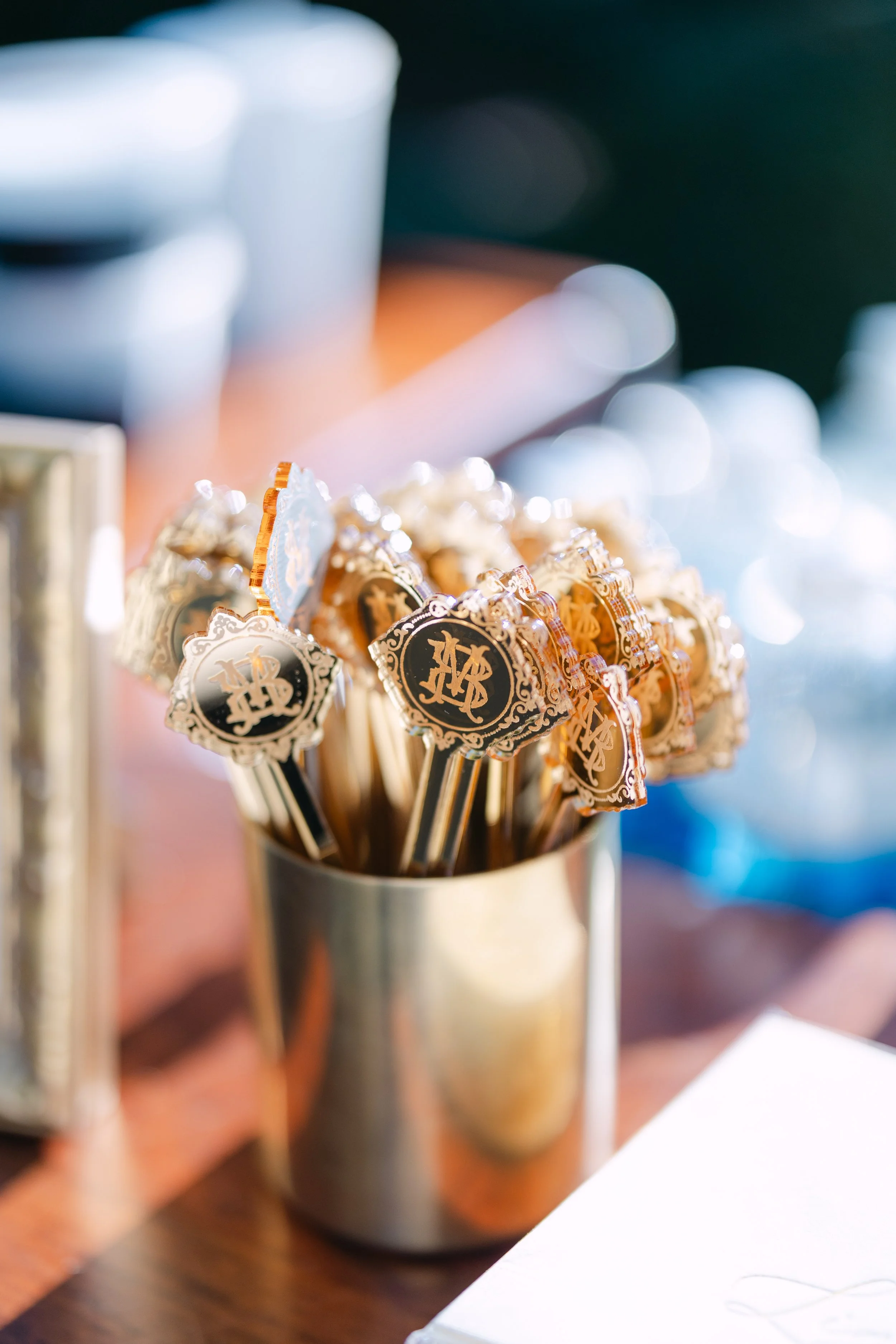 A metal cup filled with small, ornate lollipops with black and gold labels that read 'ML' or similar initials.