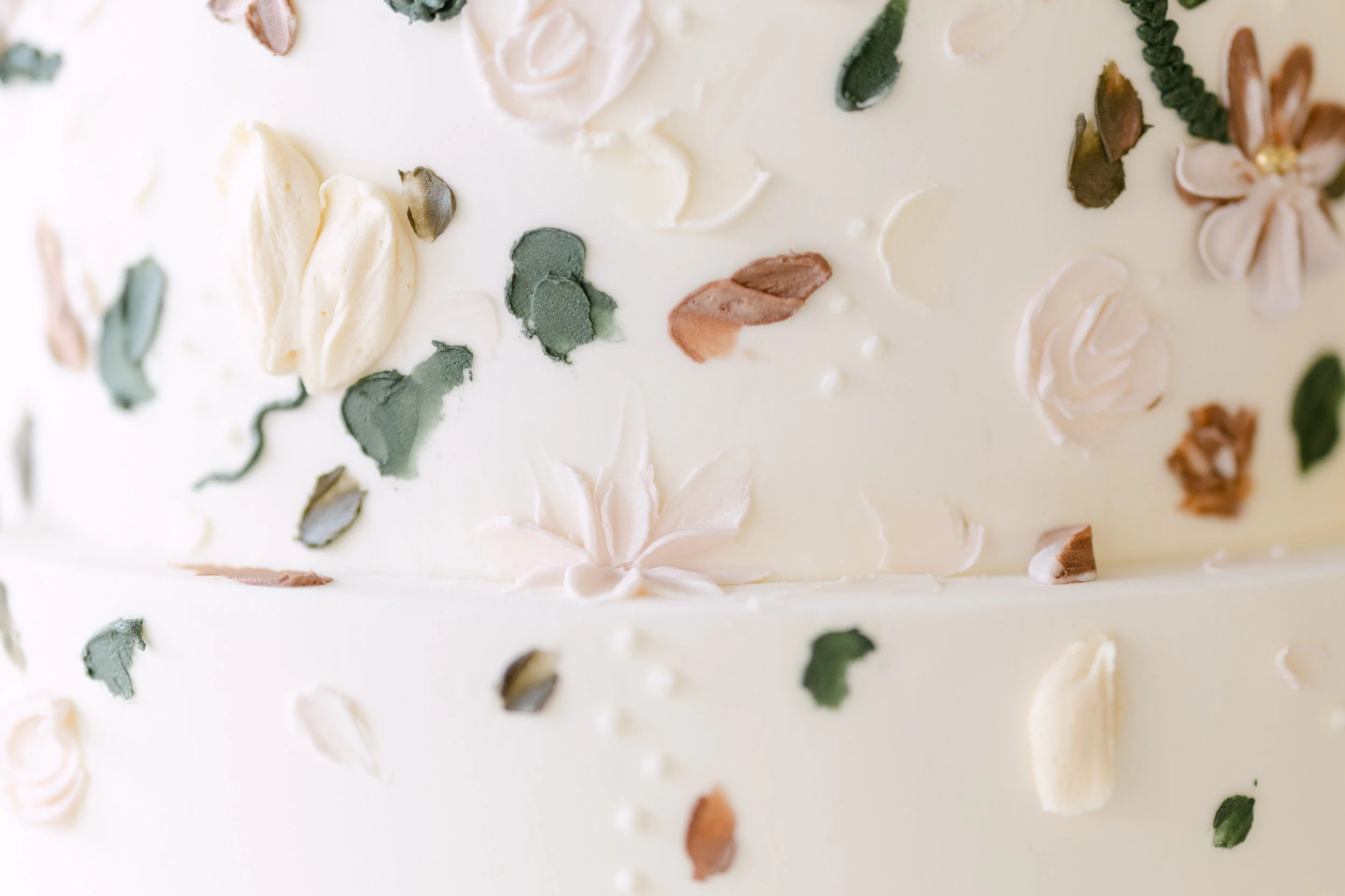 Close-up of a white cake decorated with pastel-colored flower and leaf-shaped icing decorations.