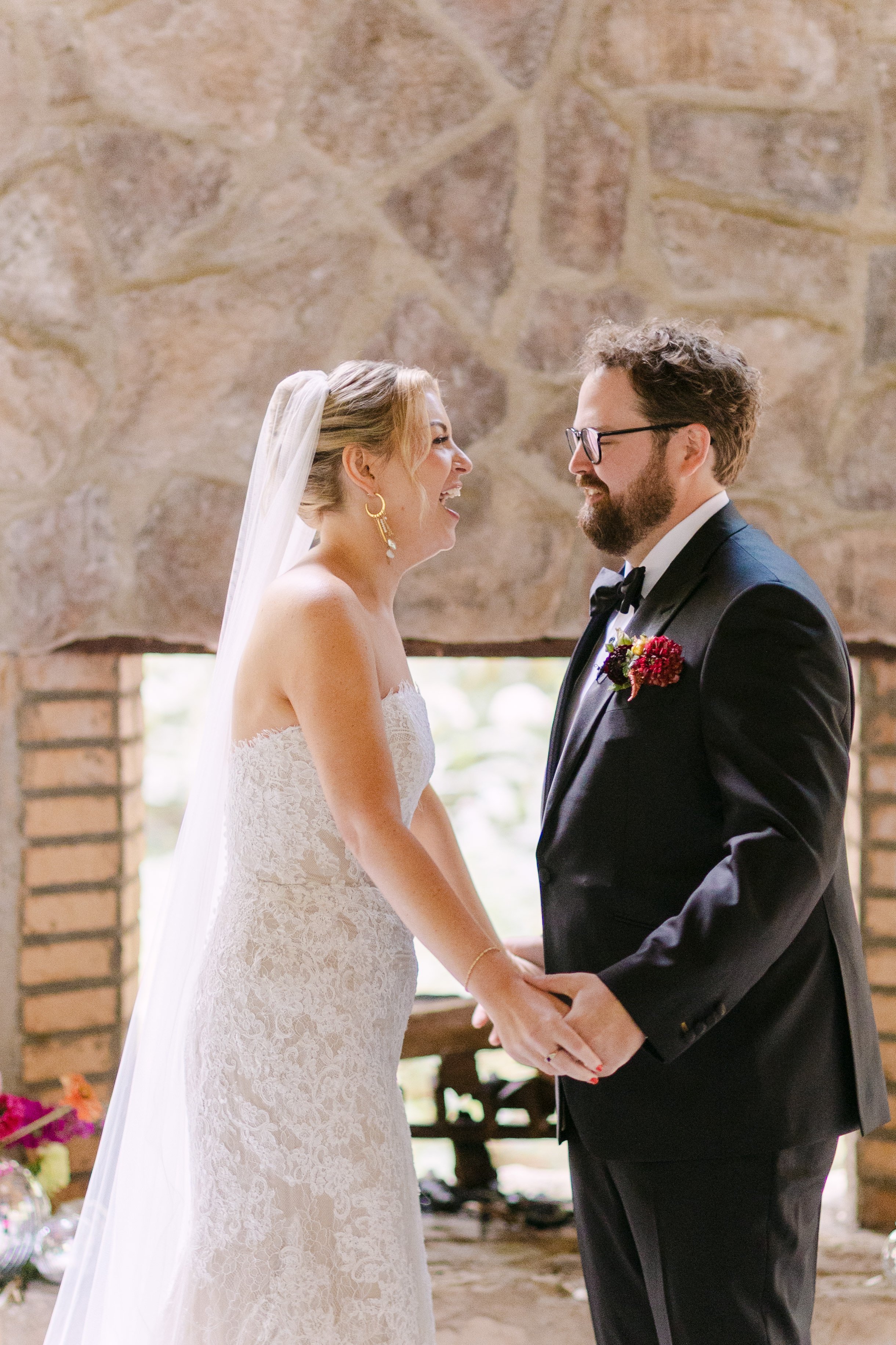 A bride and groom smiling and holding hands during their wedding ceremony indoors.