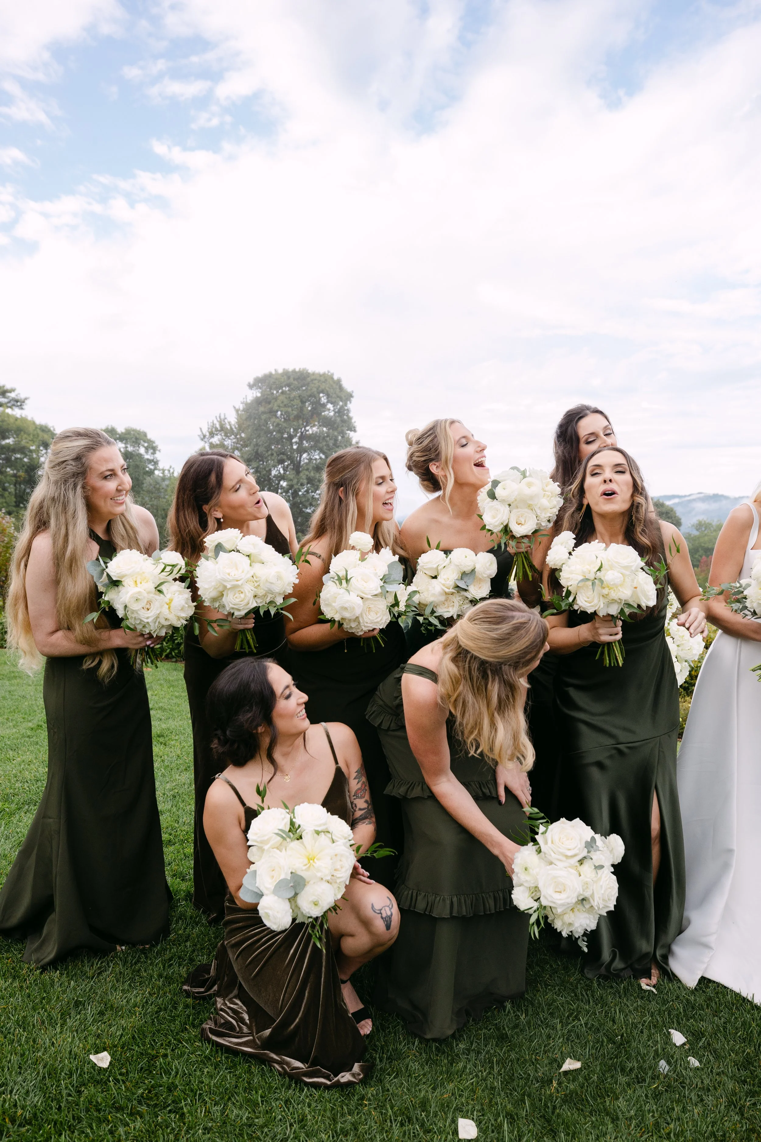 A group of women in black dresses holding white bouquets at an outdoor wedding ceremony.