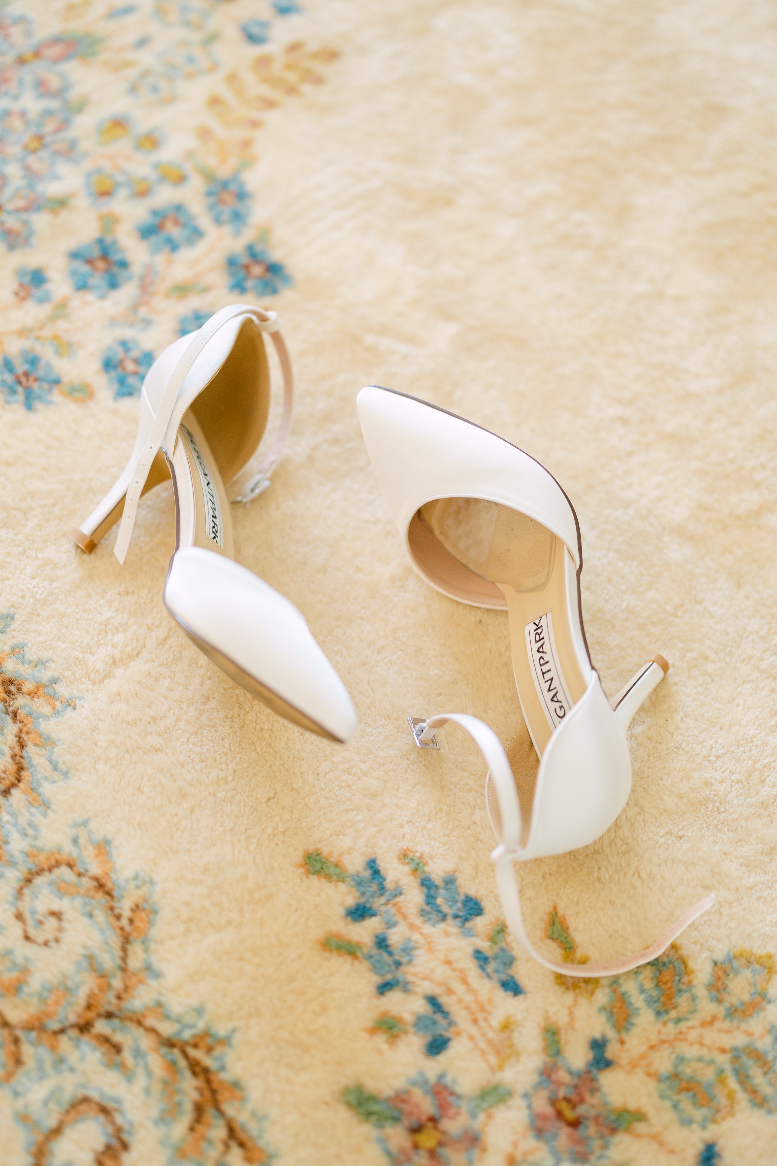 A pair of white high-heeled shoes on a decorative patterned rug.