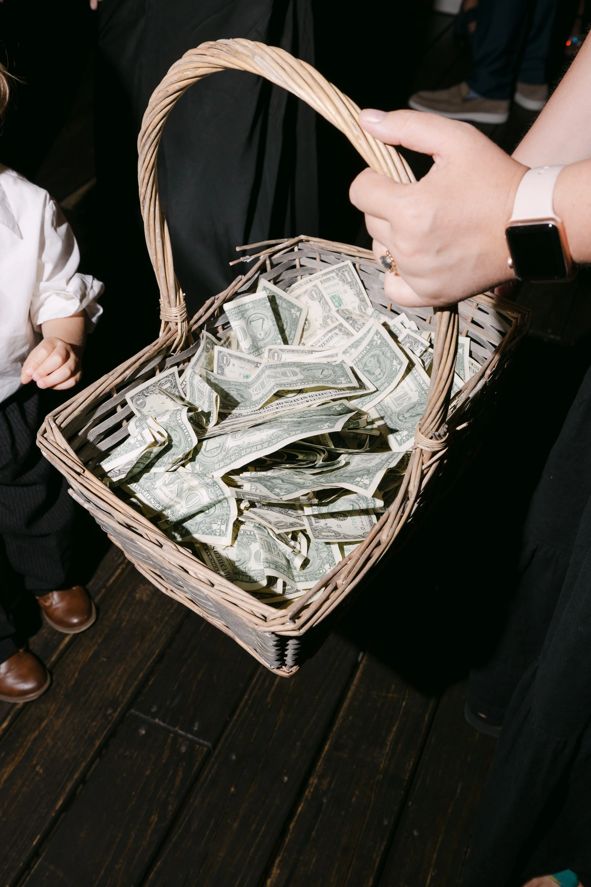 Person holding a basket filled with crumpled one-dollar bills, with a child nearby.