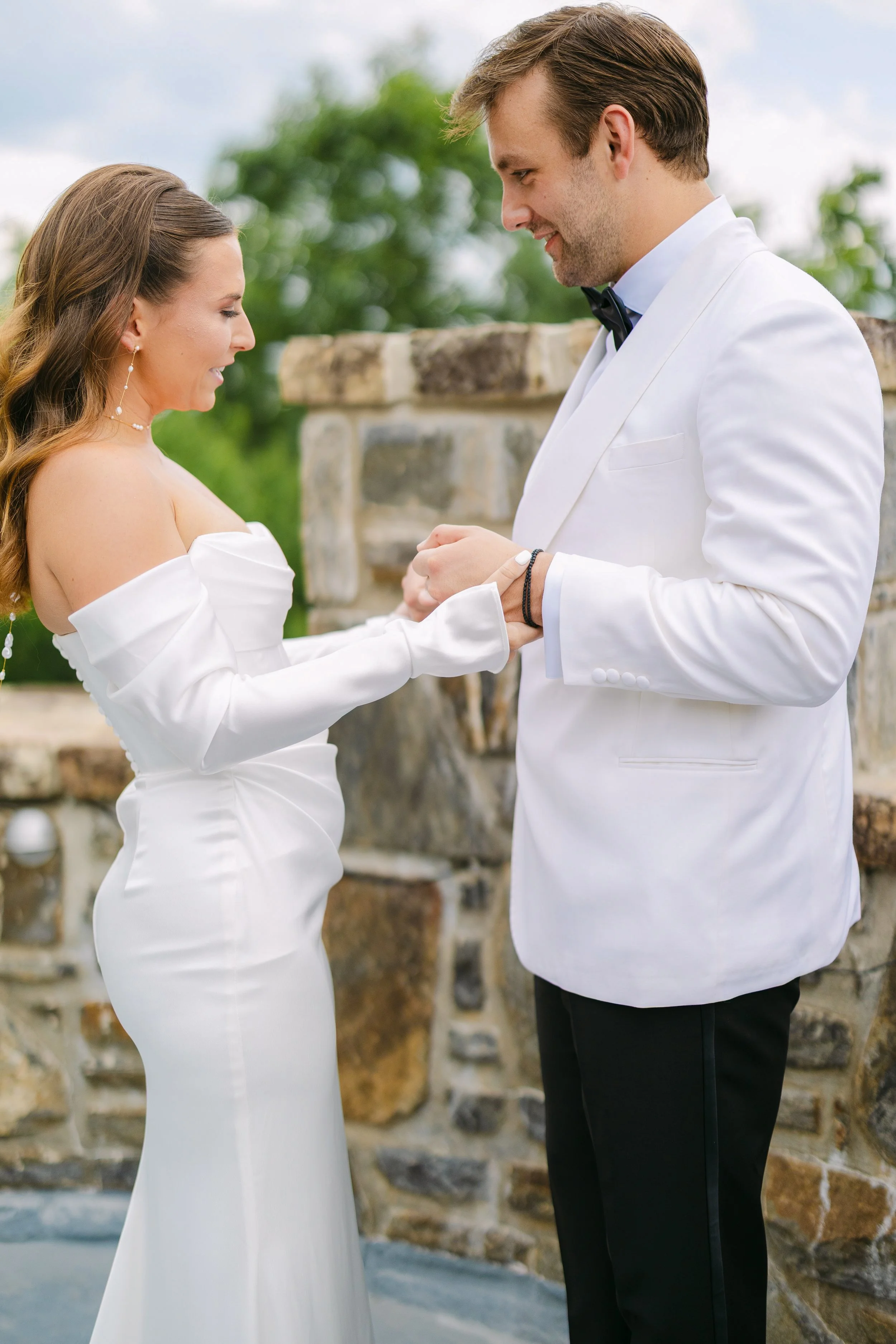 A bride and groom sharing a moment during their wedding ceremony outdoors, holding hands and looking at each other.