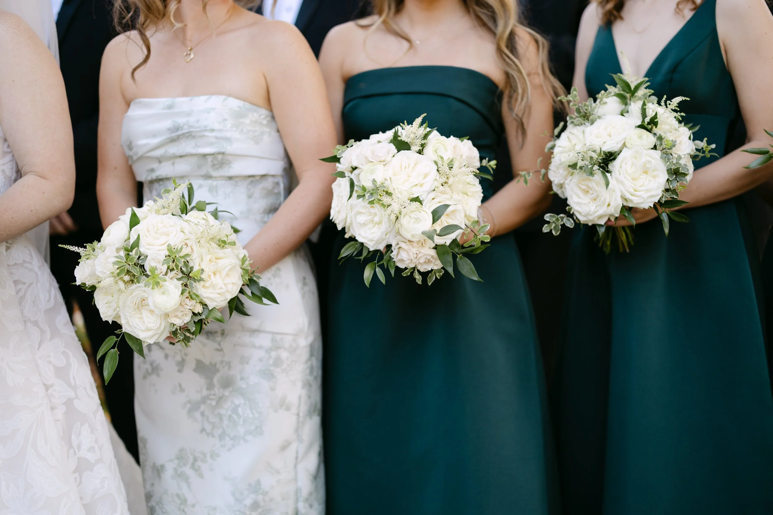 Group of women in formal dresses holding white bouquets at a wedding or special event.