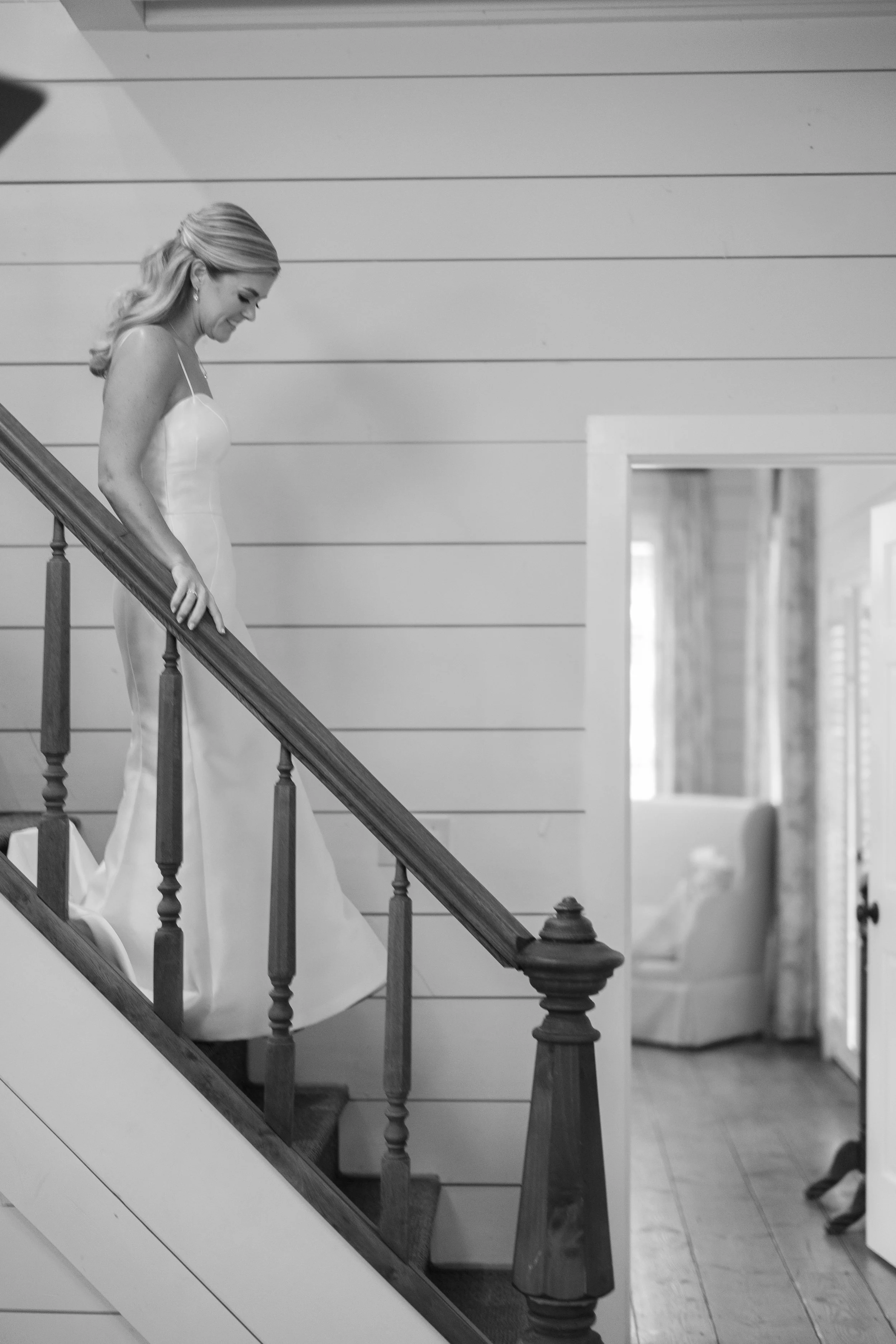 A woman in a wedding dress walking down stairs inside a house.