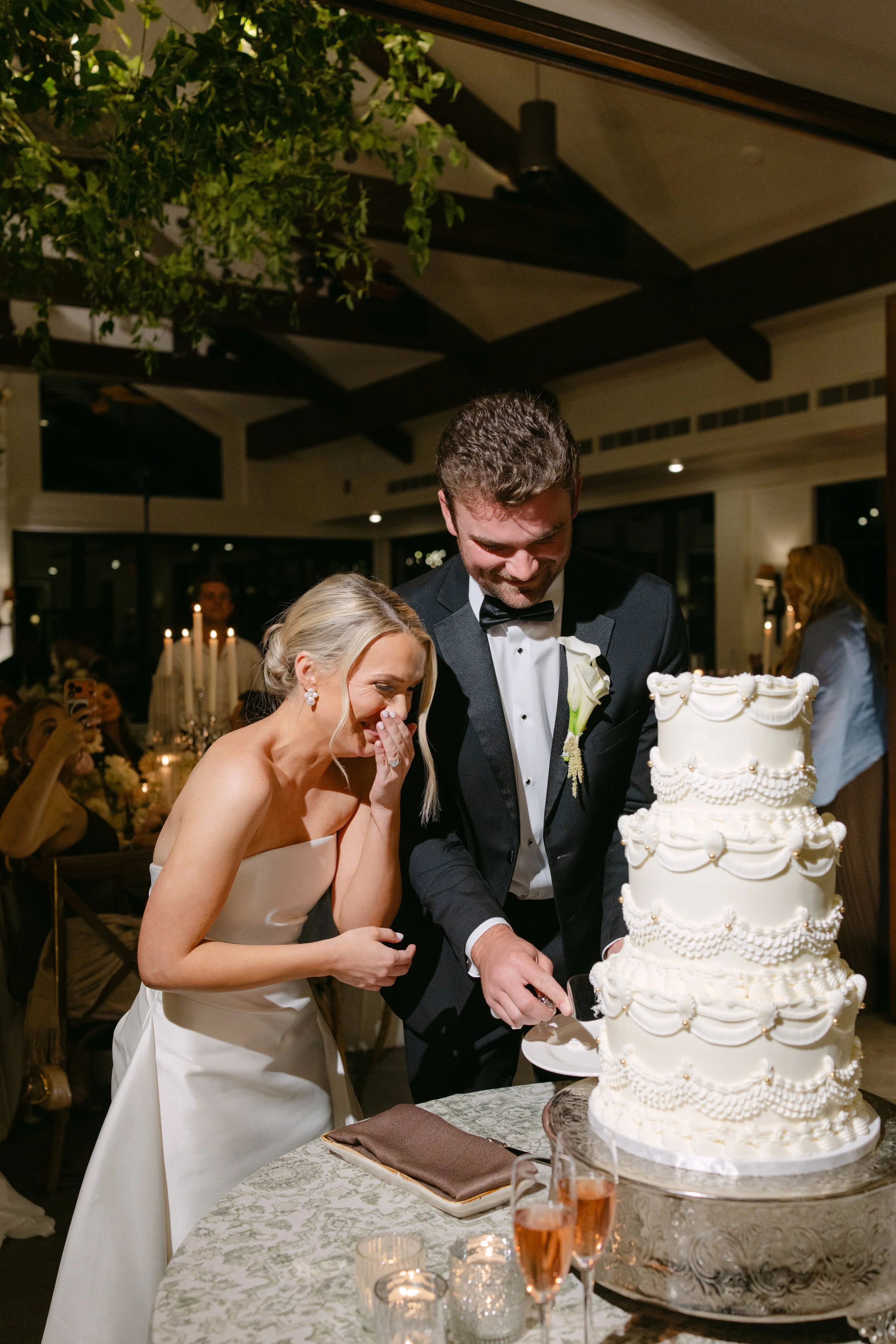 Bride and groom cutting an ornate white wedding cake at a candlelit reception