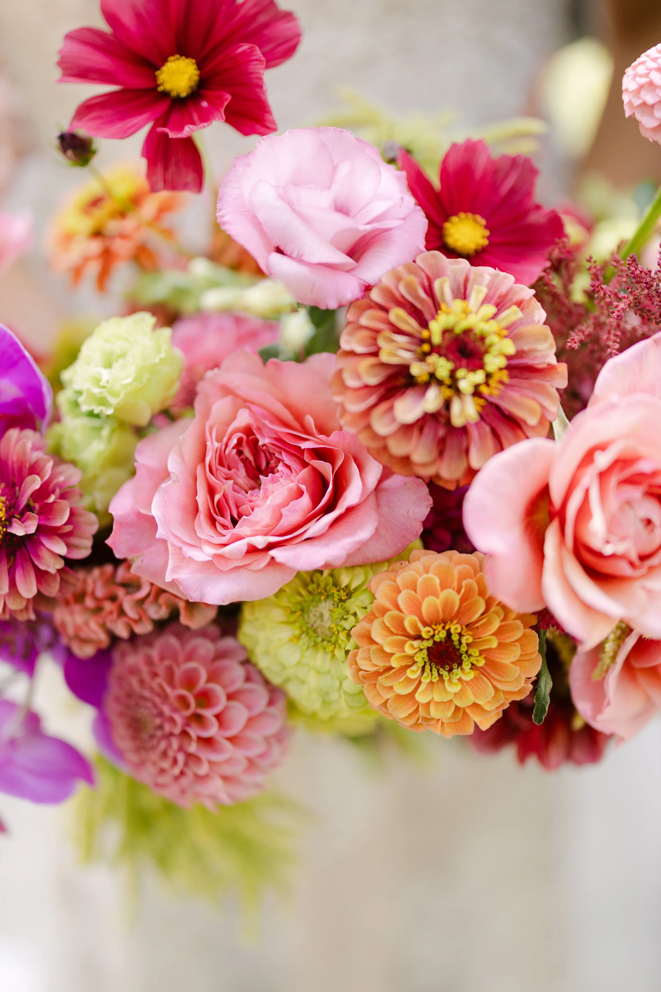 Close-up of a colorful bouquet of various pink, red, orange, purple, and cream flowers including roses, dahlias, and zinnias.