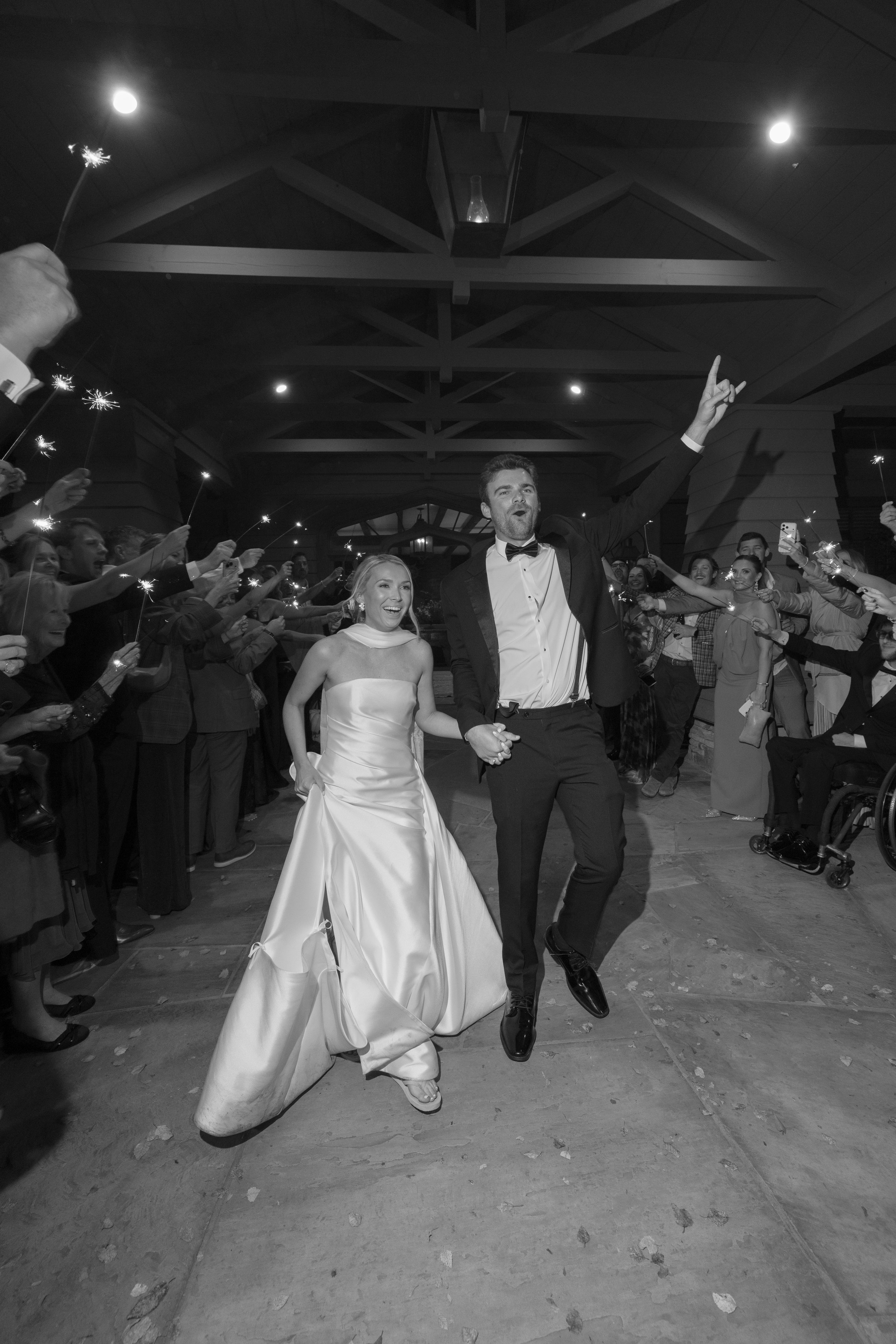 Bride and groom celebrate their wedding exit as guests hold sparklers in a rustic reception venue.