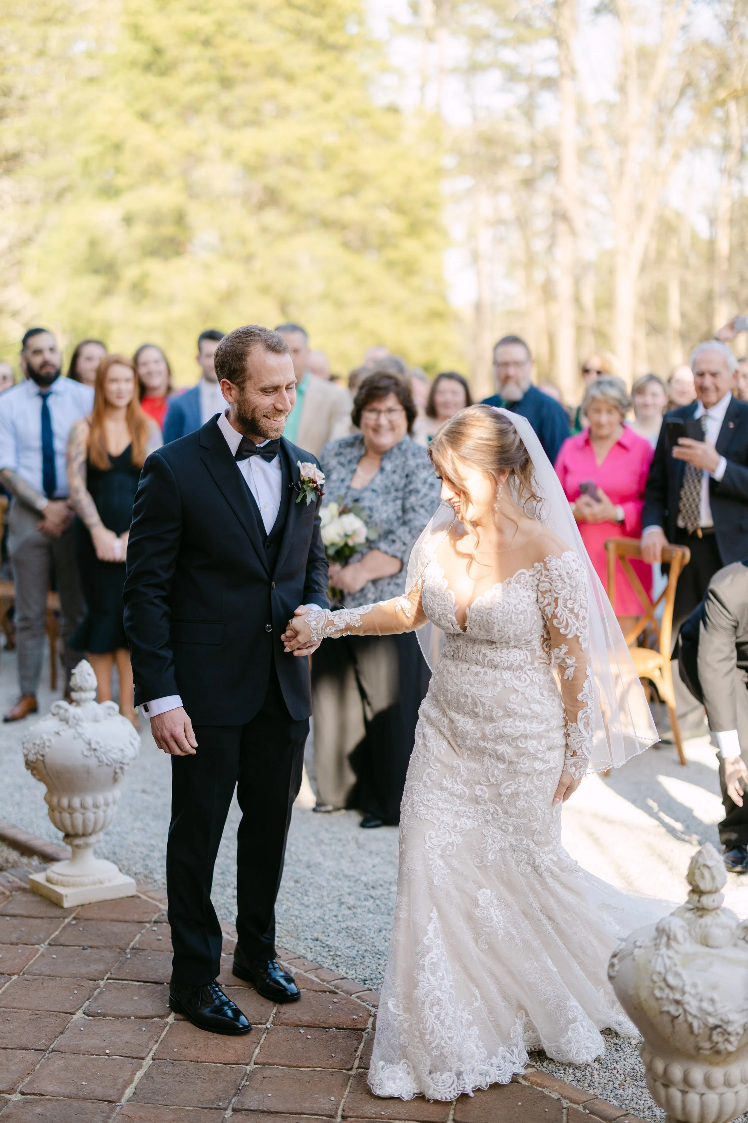 Bride and groom holding hands at their outdoor wedding ceremony with guests in the background.