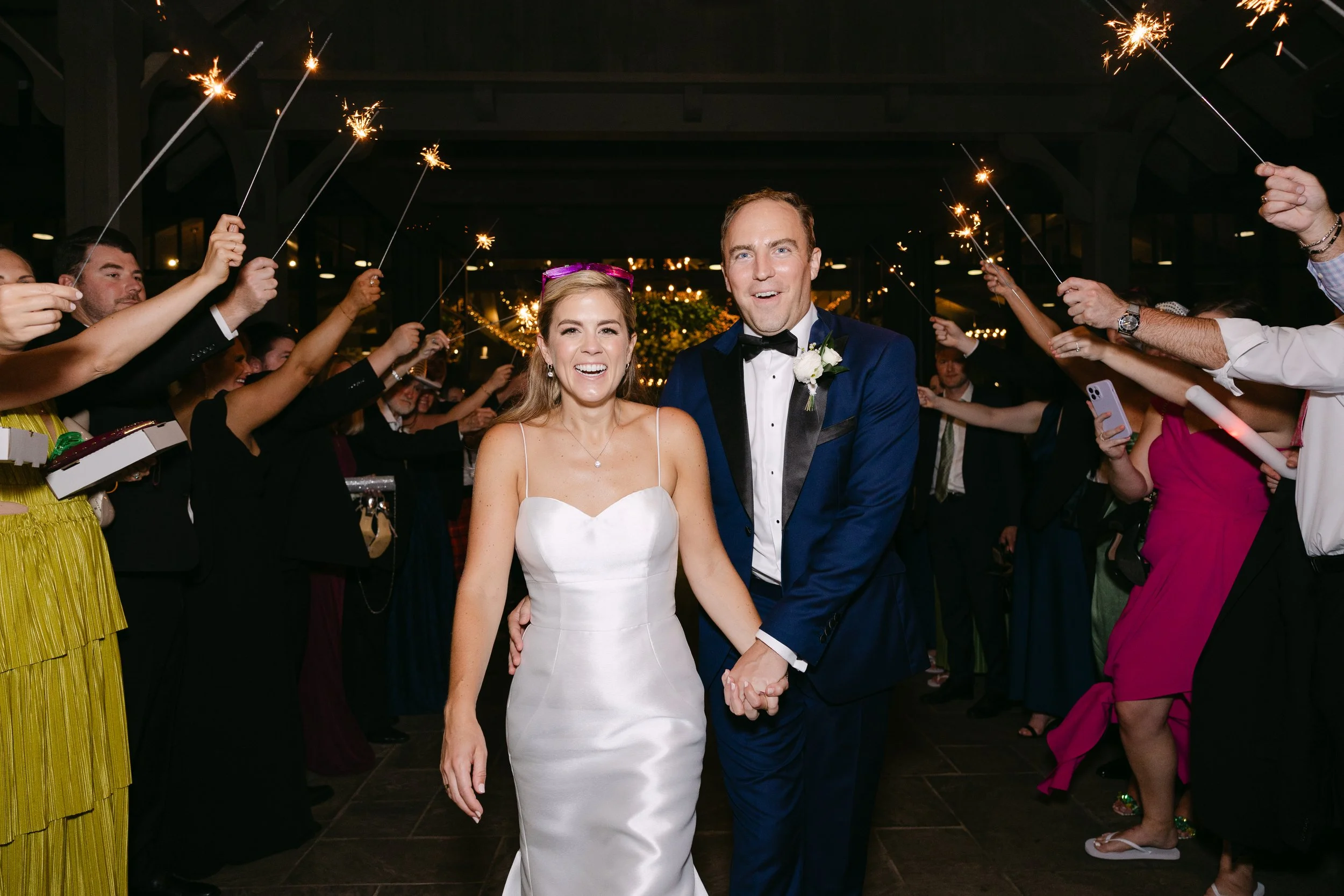 Wedding couple walking hand in hand through guests holding sparklers during celebration.