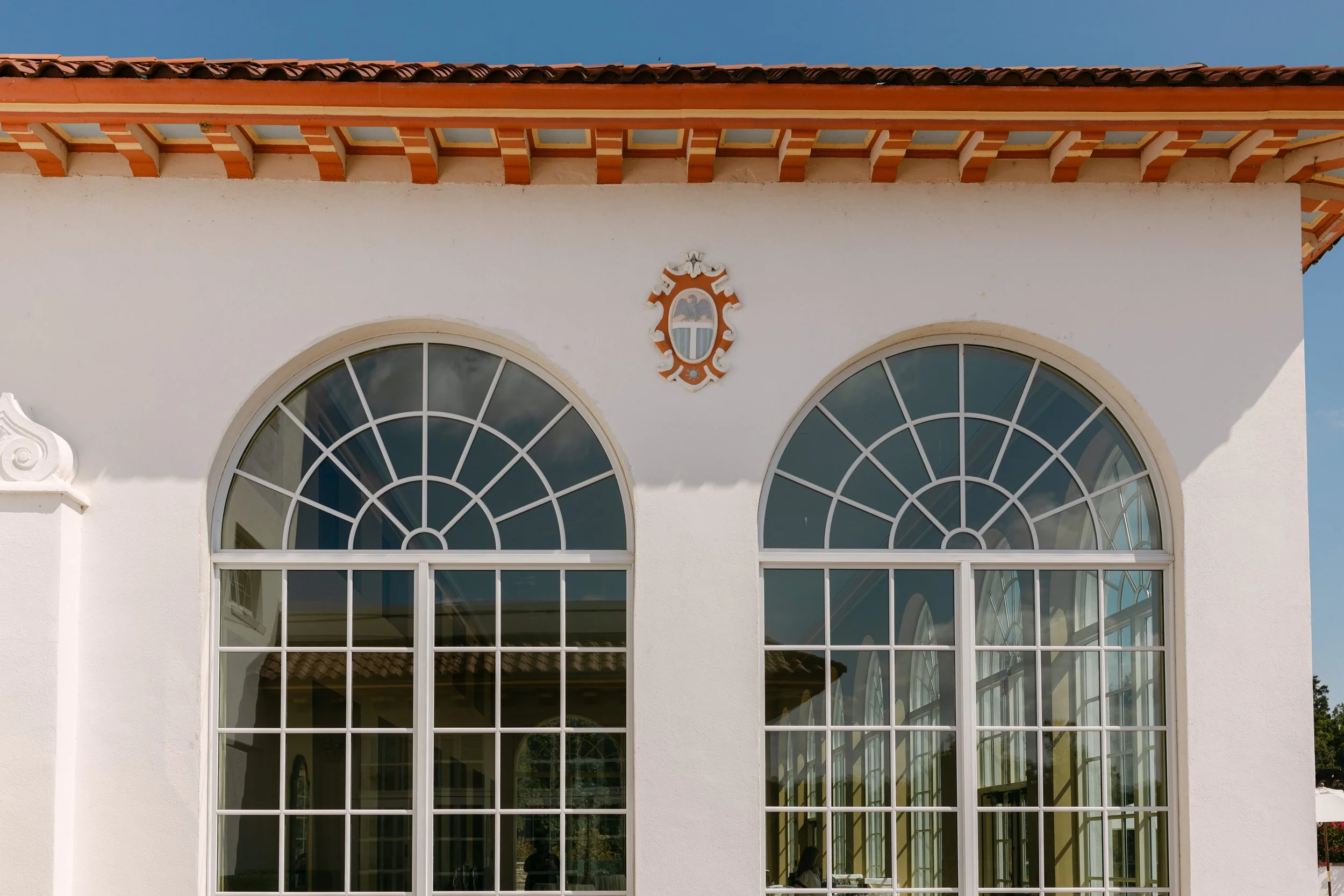 Front of a white building with large arched windows and a decorative crest centered above the windows.